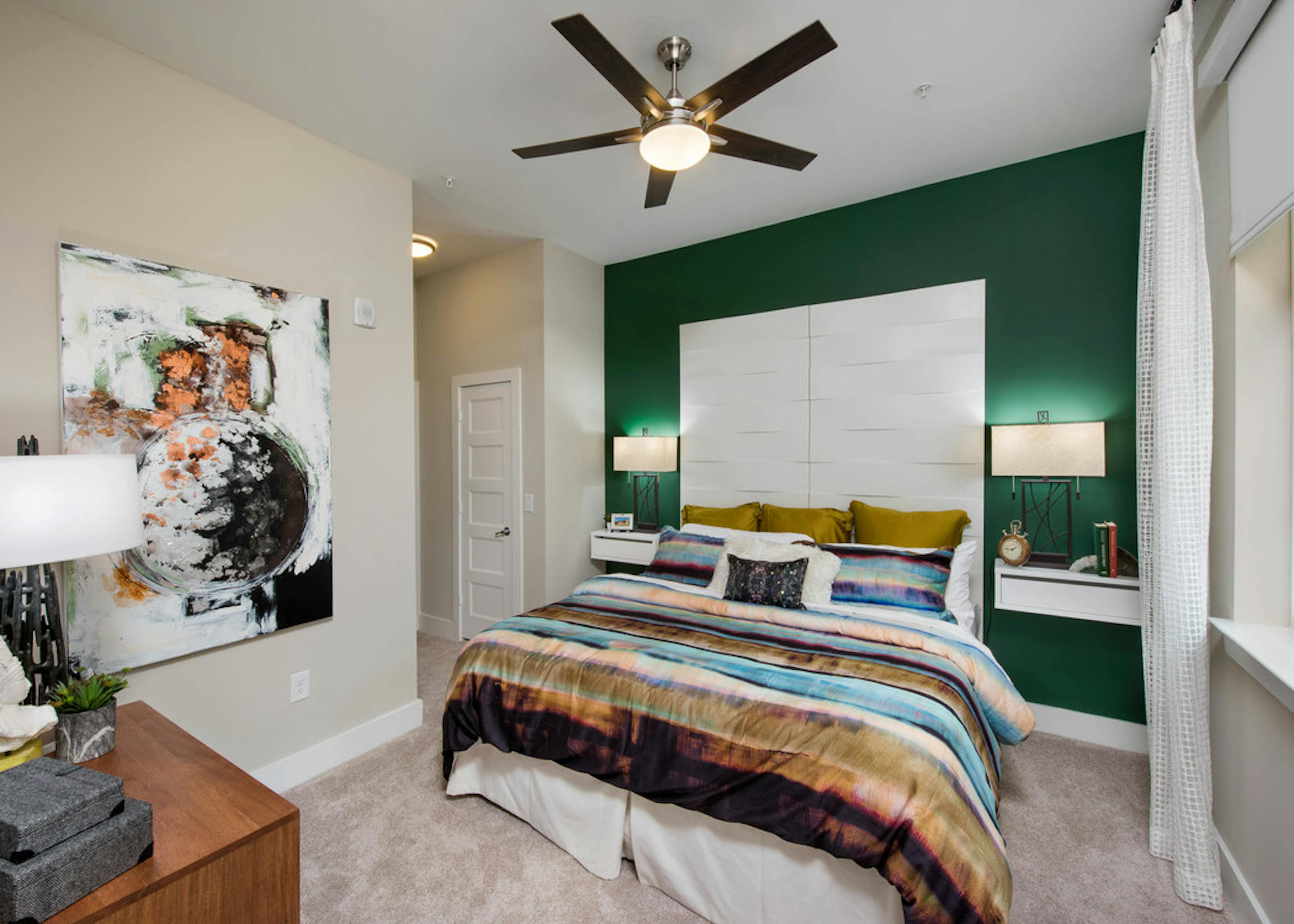 AMLI Buckhead bedroom with emerald accent wall and teal, coral and olive striped bedding with window to the right of the bed