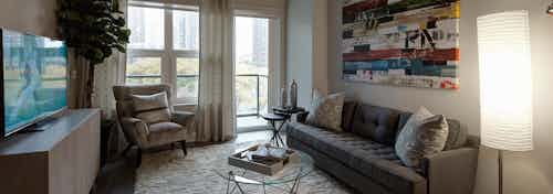 Living room at AMLI Lofts with grey and white furnishings paired with colorful wall art and a glass door leading to a balcony
