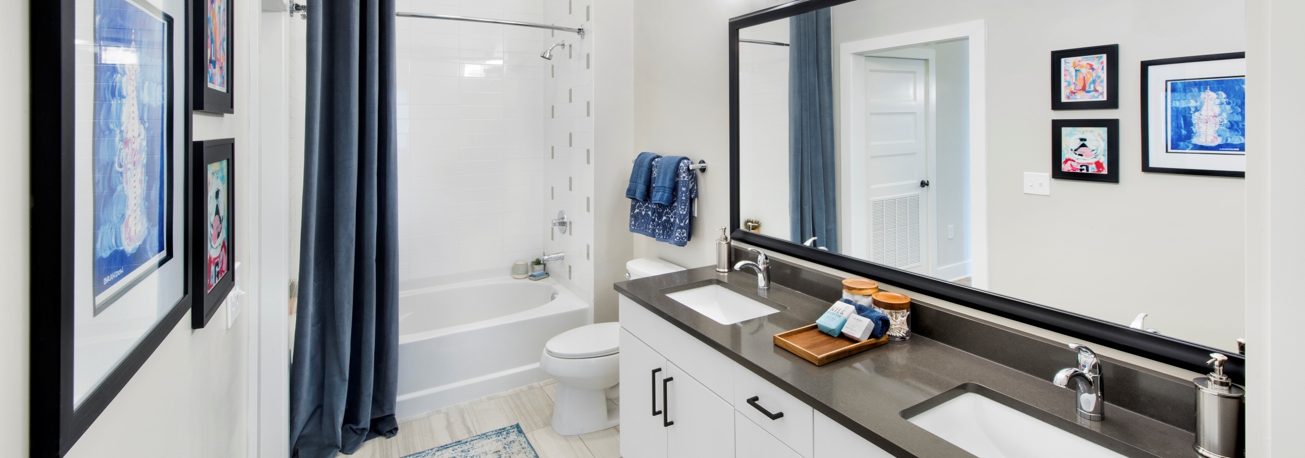 AMLI Decatur bathroom with a double vanity with white cabinets and dark countertops with a soaking tub and framed mirror