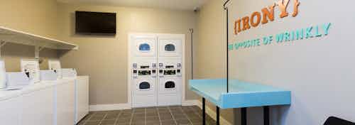 AMLI Campion Trail laundry room with washing machines at left and dryers in back and overhead TV and folding table on right
