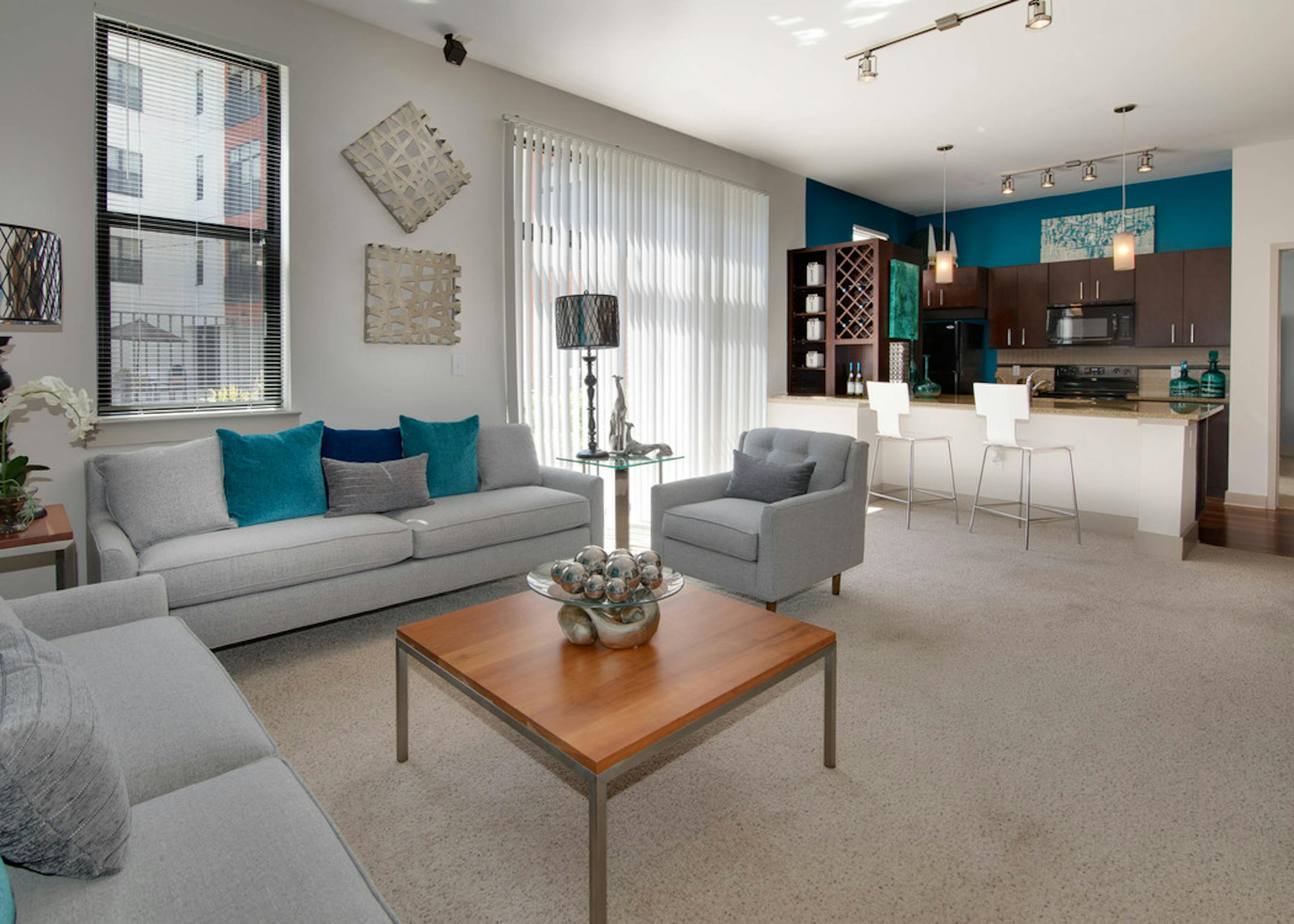 AMLI Old 4th Ward living room with grey seating and neutral carpet flooring leading to kitchen in the background