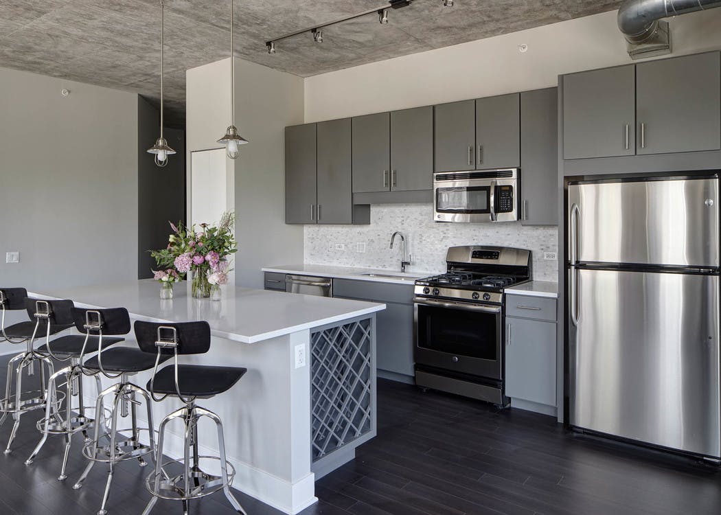 An AMLI Lofts kitchen which is painted gray and white and has an island with quartz countertops and four black bar stools