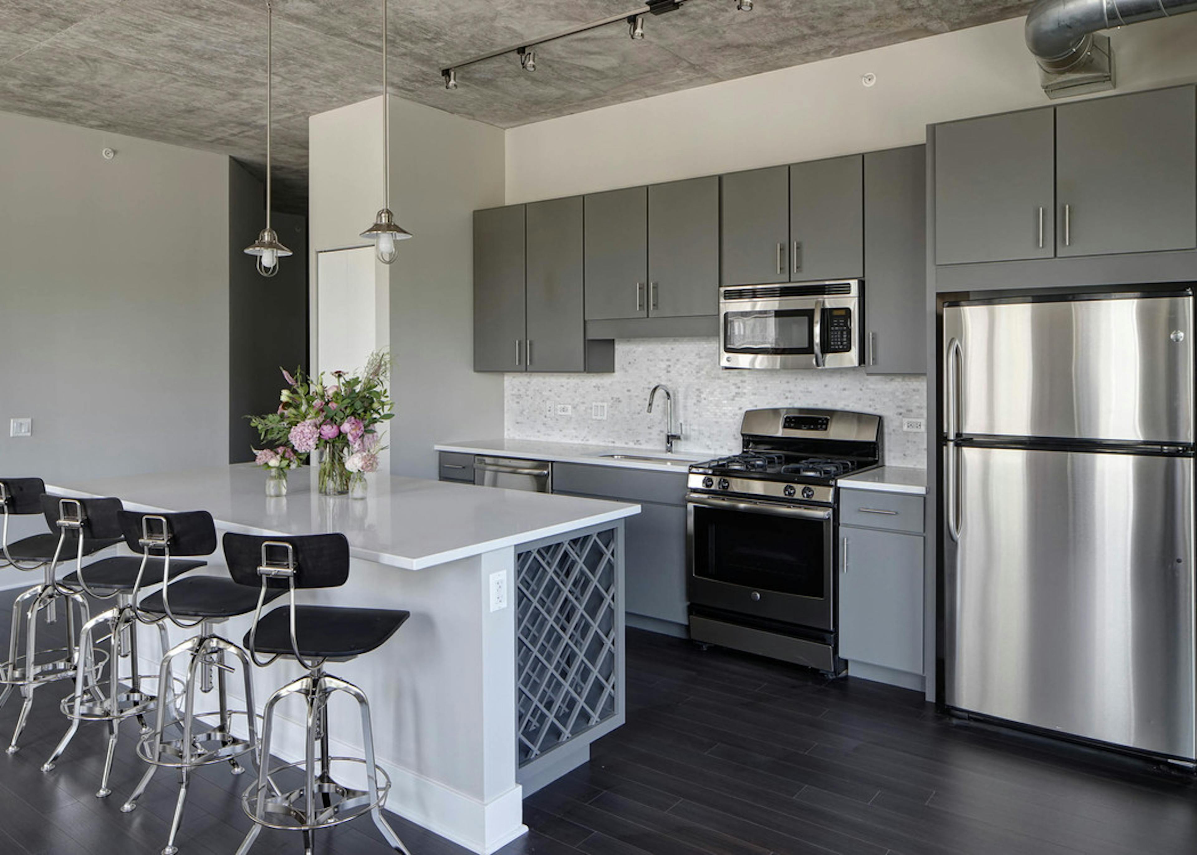 An AMLI Lofts kitchen which is painted gray and white and has an island with quartz countertops and four black bar stools