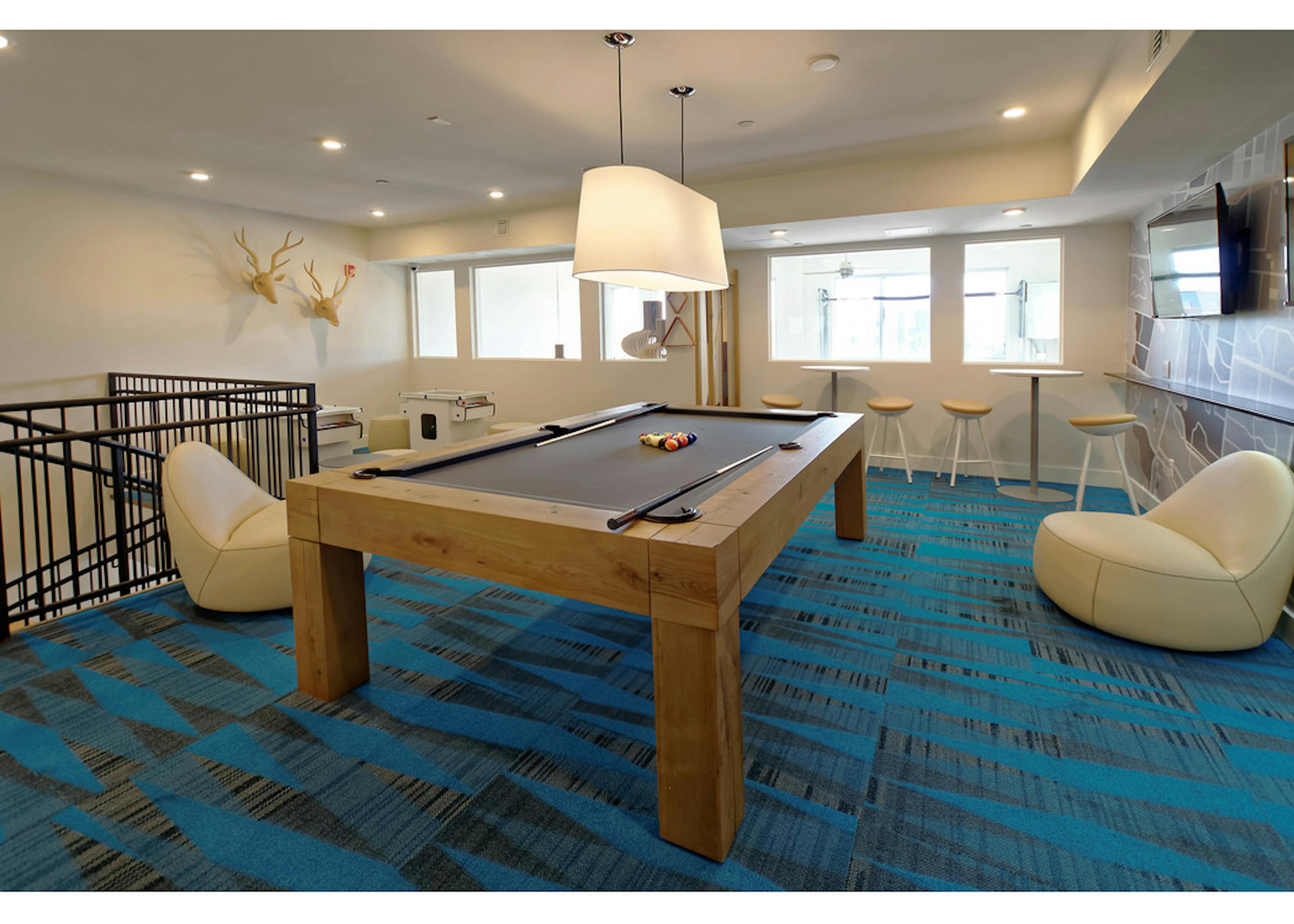 Interior view of a resident lounge at AMLI Dry Creek apartments with a dining table a kitchen area and a spiral staircase 