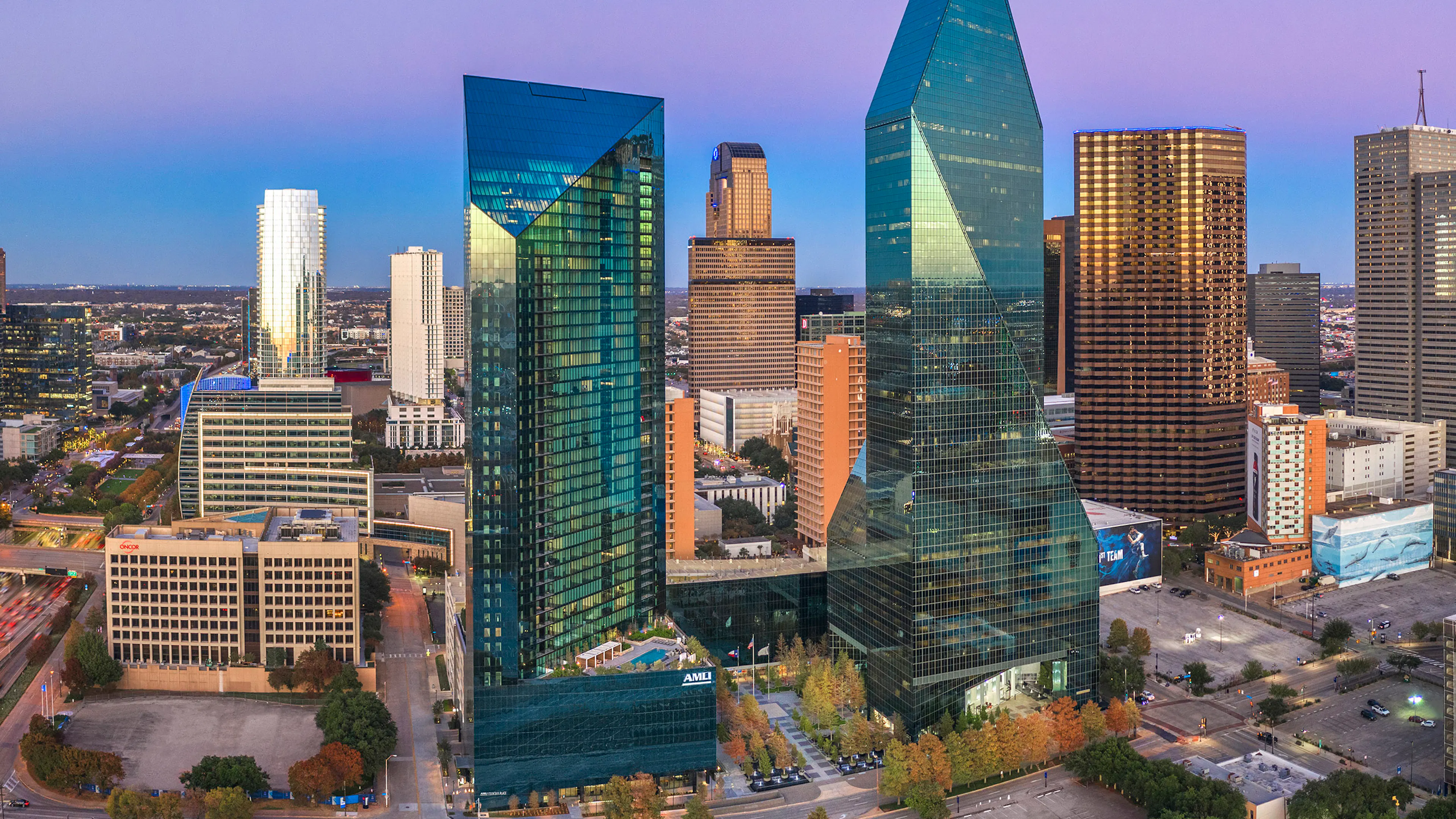 Dusk aerial view of AMLI Fountain Place apartment building and Fountain Place office building with blue and purple sky