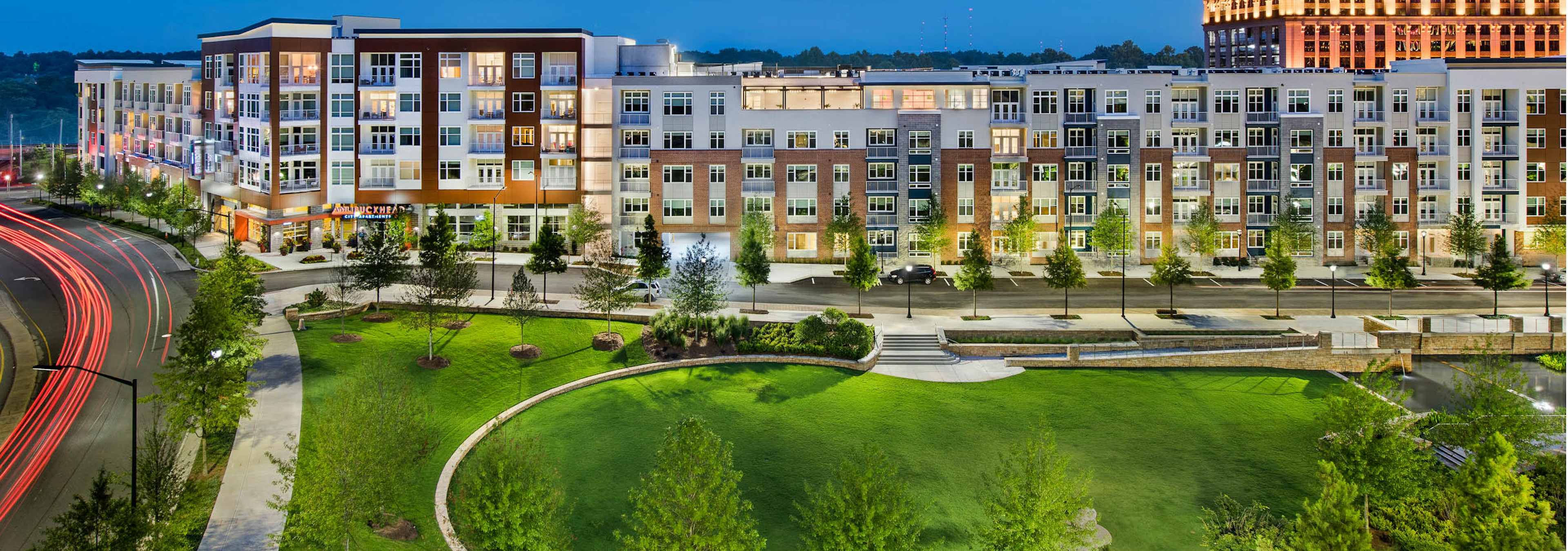 Exterior of AMLI Buckhead apartment community at night with light coming through the windows and trees lining the sidewalk