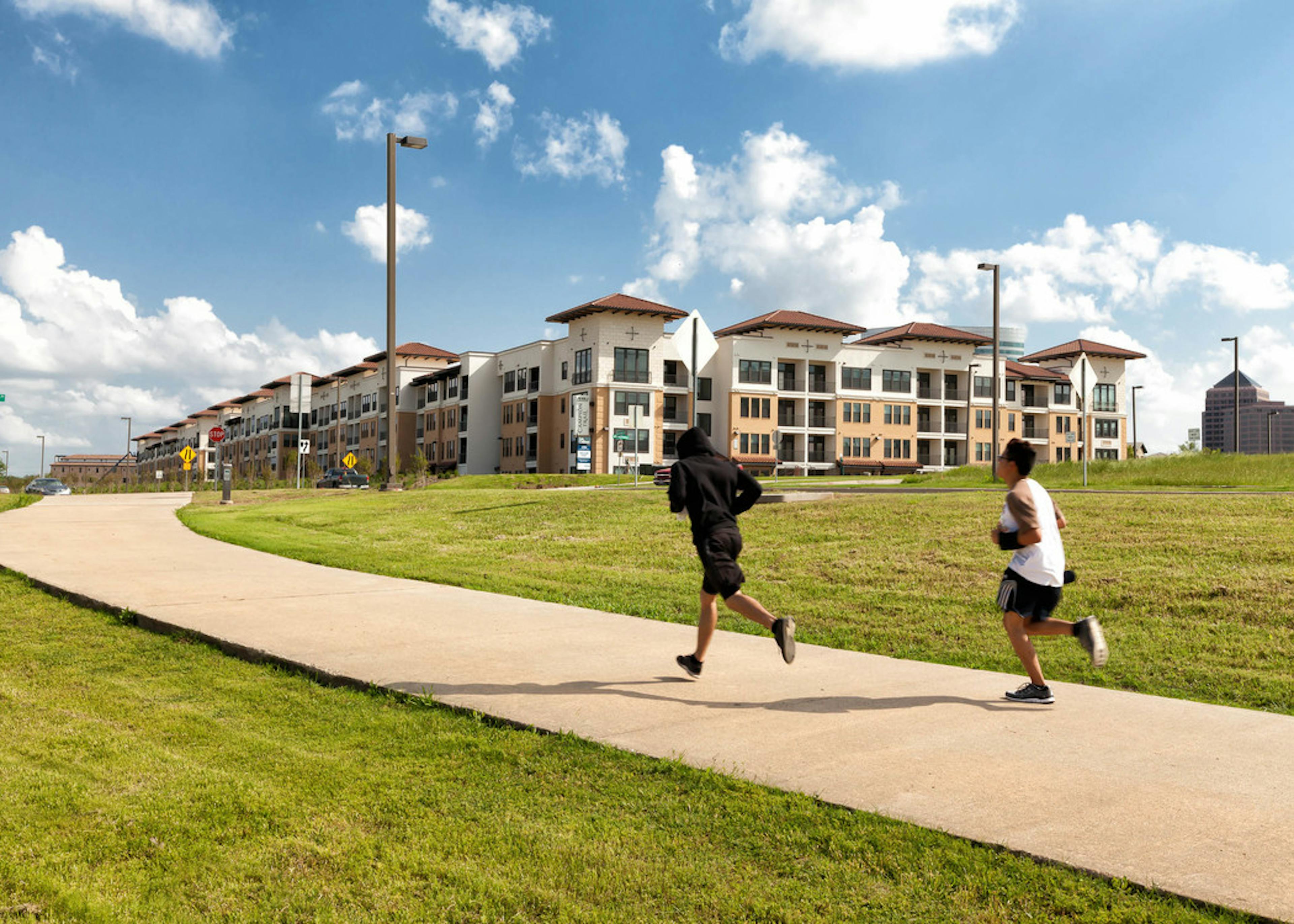 Joggers on concrete path with grass on either side of them and AMLI Campion Trail apartment building in the distance