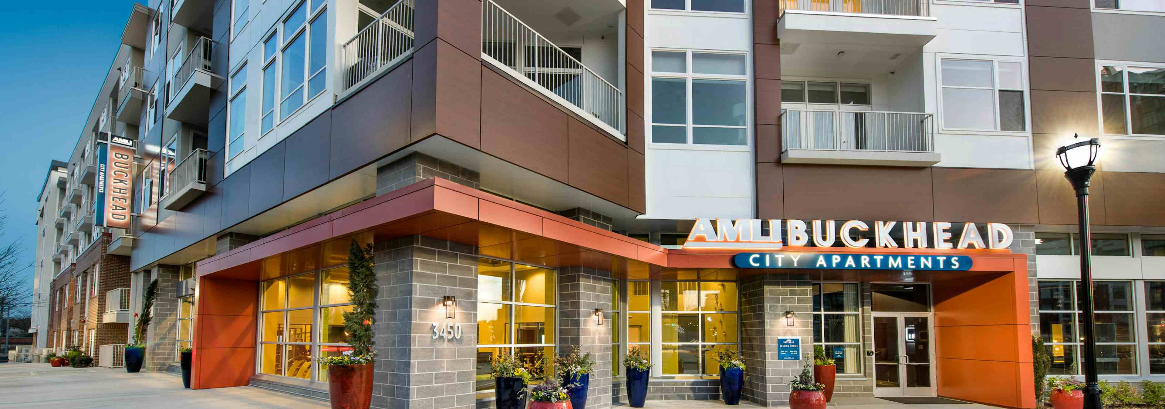 AMLI Buckhead exterior facade with a grey brick and orange entryway with potted plants and white balconies on floors above