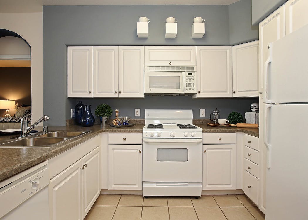 Interior of AMLI Warner Center apartment kitchen with white cabinetry, double sink and white appliances and peek into bedroom