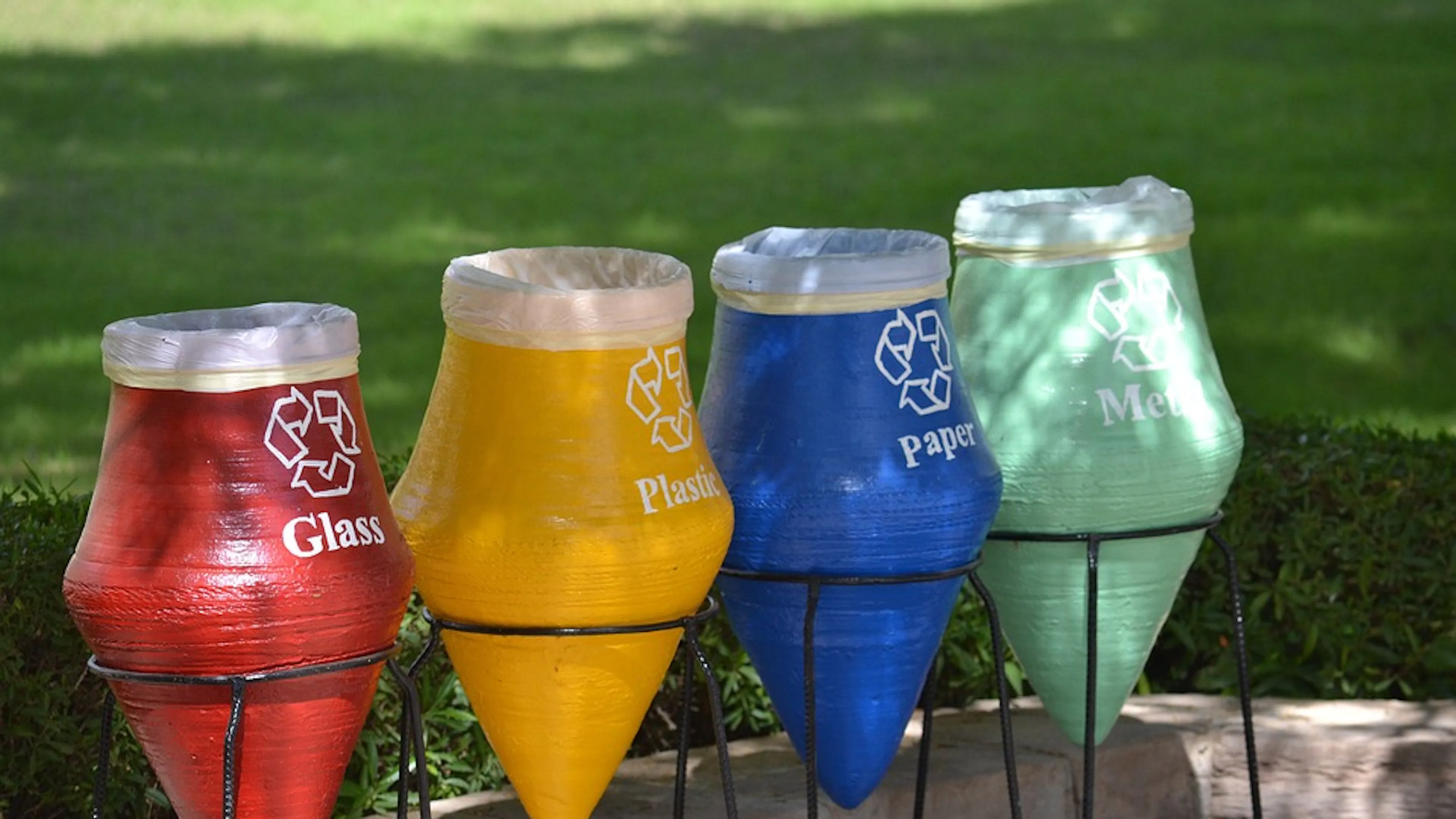 Four recycling bins next to each other in red blue yellow and green with the words glass plastic paper and metal on them