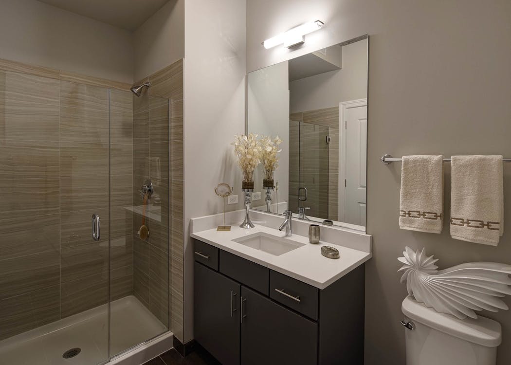 Bathroom at AMLI Lofts with taupe decor and a single vanity as well as a beige tiled shower with a clear glass door