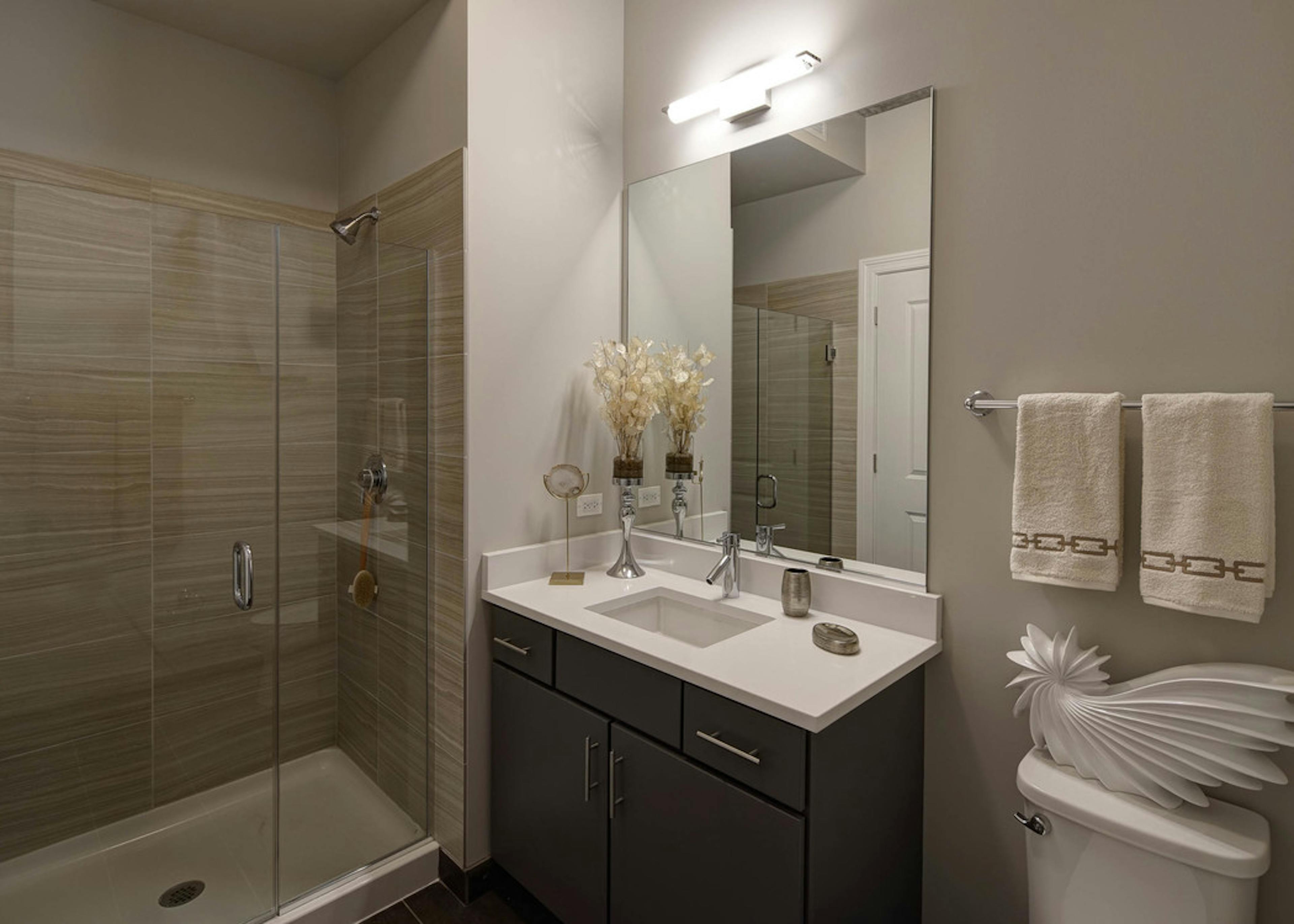 Bathroom at AMLI Lofts with taupe decor and a single vanity as well as a beige tiled shower with a clear glass door
