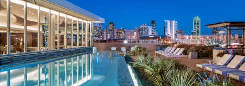 Nighttime view of AMLI Design District infinity-edge swimming pool and lounge seating overlooking the Dallas skyline