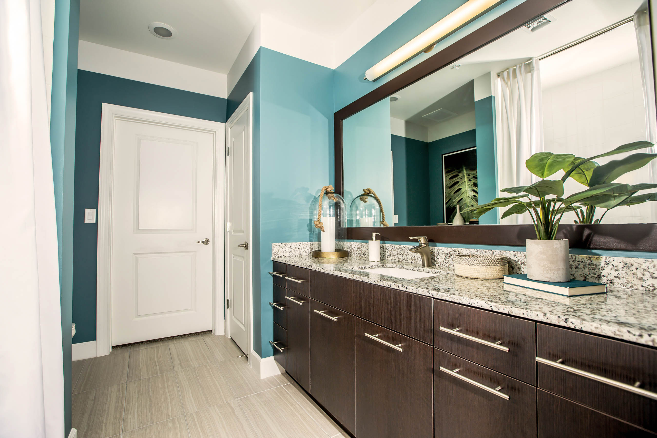 Interior view of a bathroom at AMLI Joya apartment with double sink vanity, large mirror on wall and granite counters.
