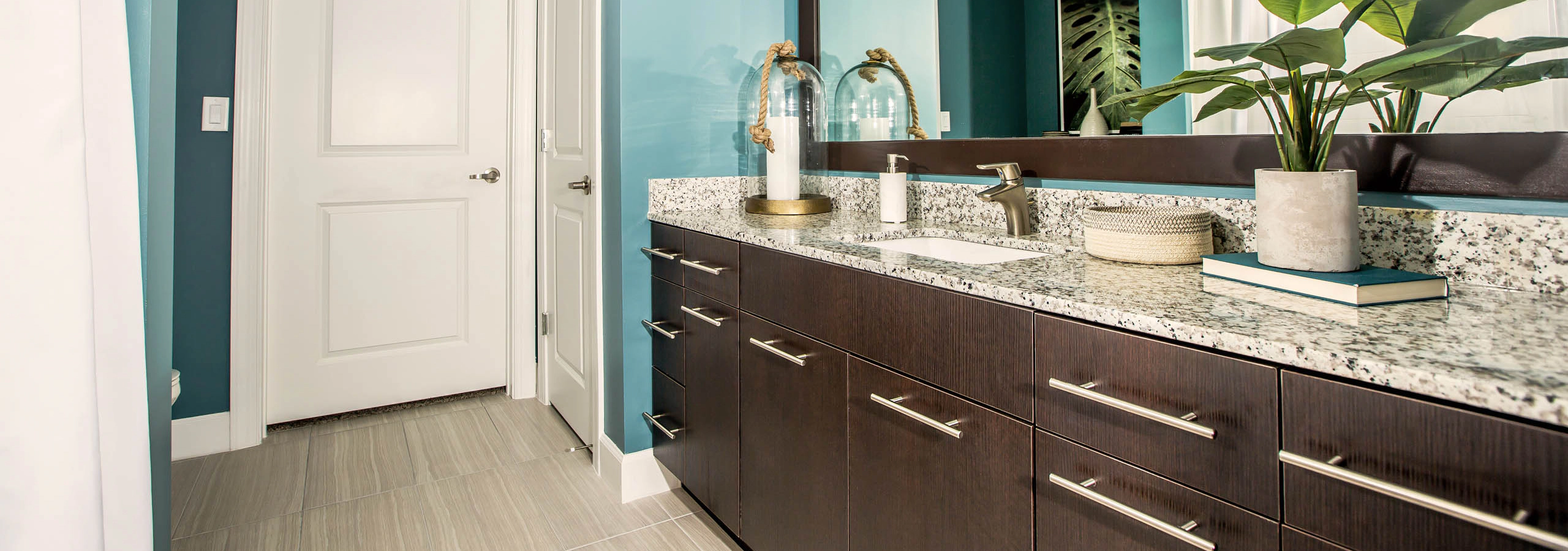 Interior view of a bathroom at AMLI Joya apartment with double sink vanity, large mirror on wall and granite counters.