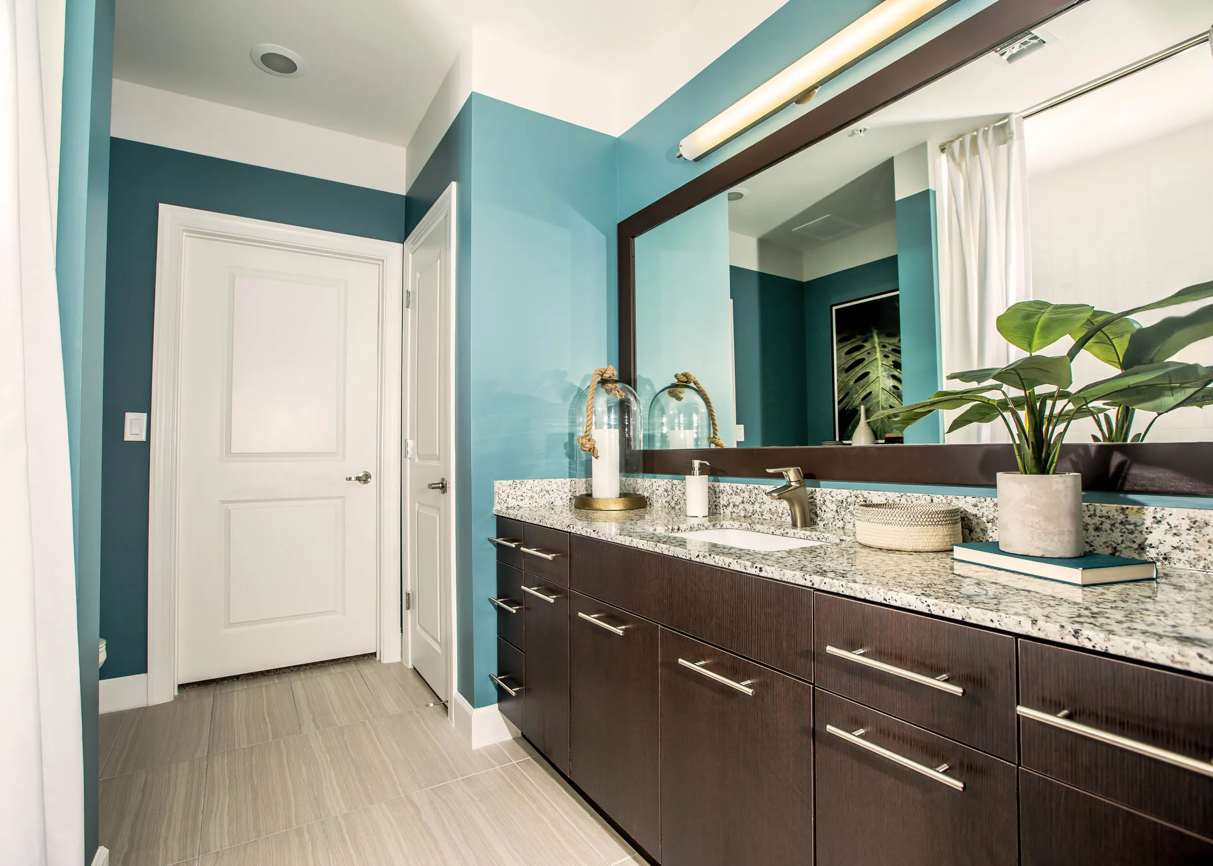 Interior view of a bathroom at AMLI Joya apartment with double sink vanity, large mirror on wall and granite counters.