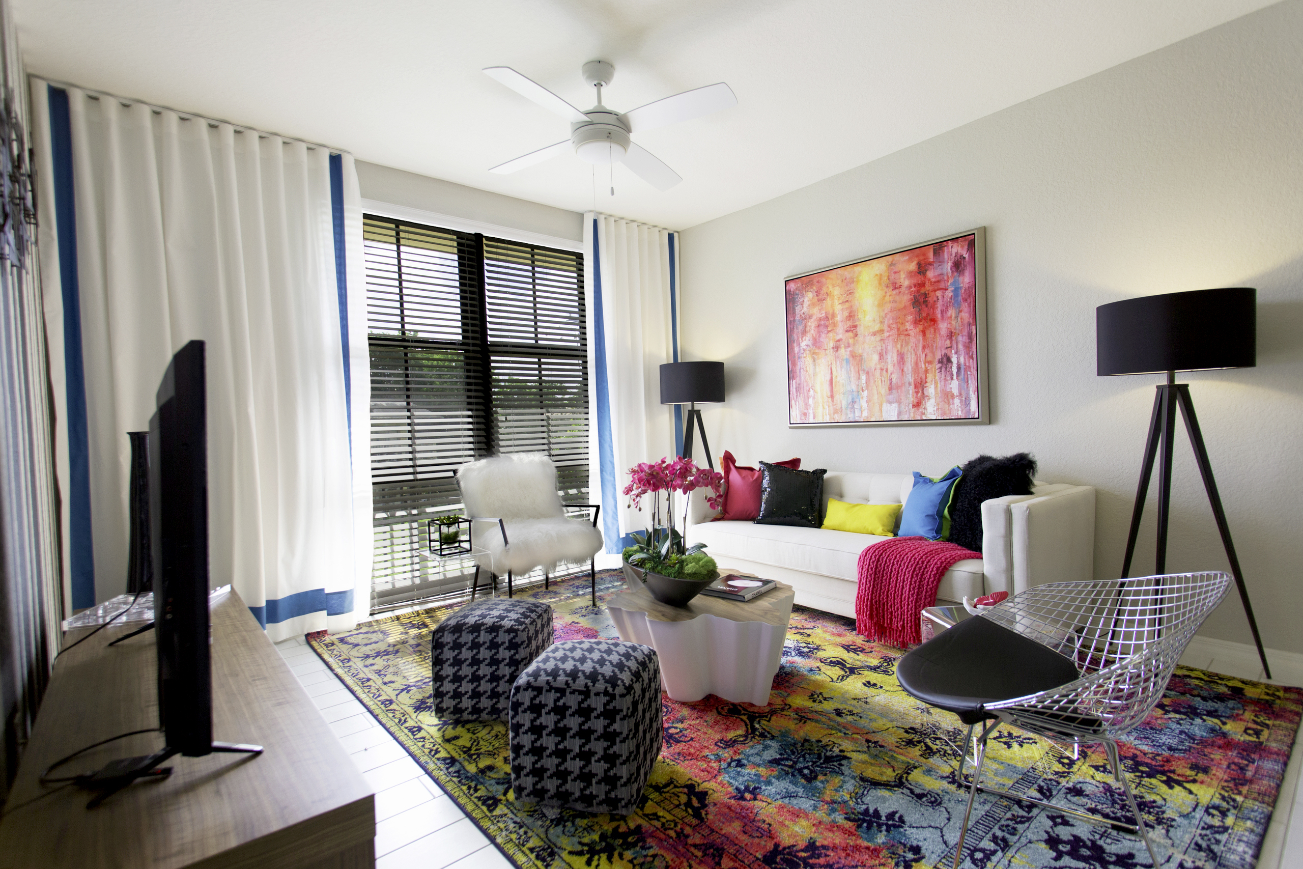 Interior of an AMLI Dadeland apartment living area with white sofa, pillows, modern colorful artwork and black floor lamps