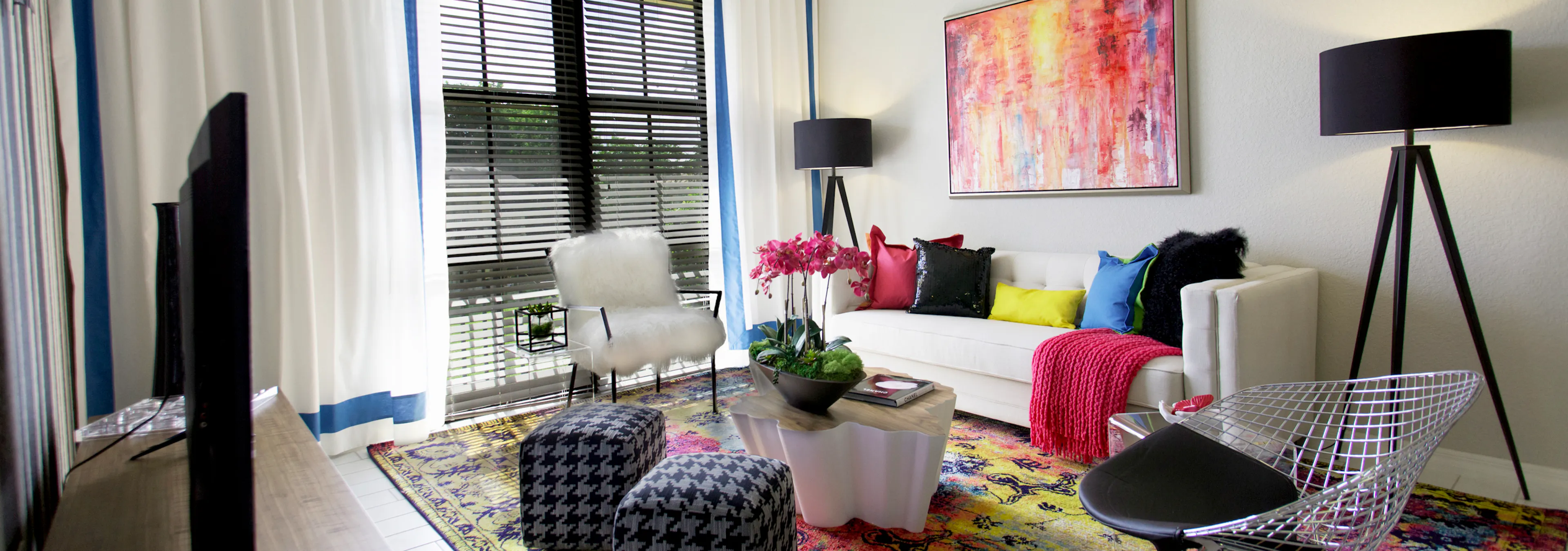 Interior of an AMLI Dadeland apartment living area with white sofa, pillows, modern colorful artwork and black floor lamps