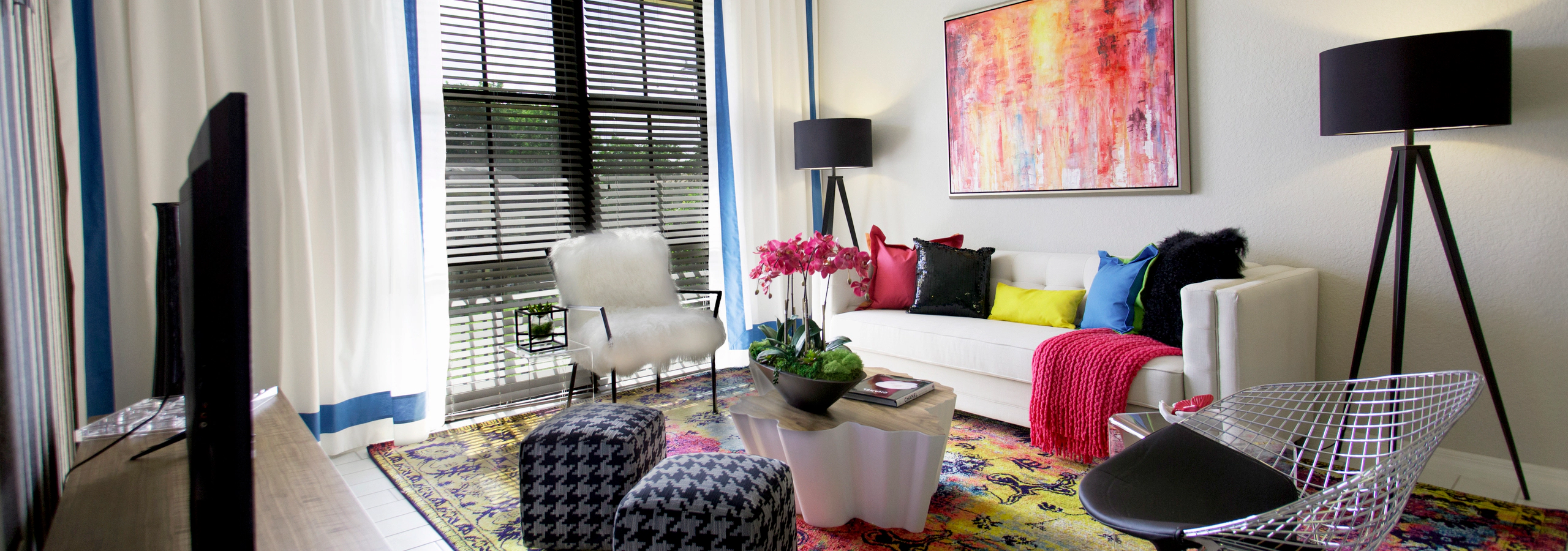 Interior of an AMLI Dadeland apartment living area with white sofa, pillows, modern colorful artwork and black floor lamps