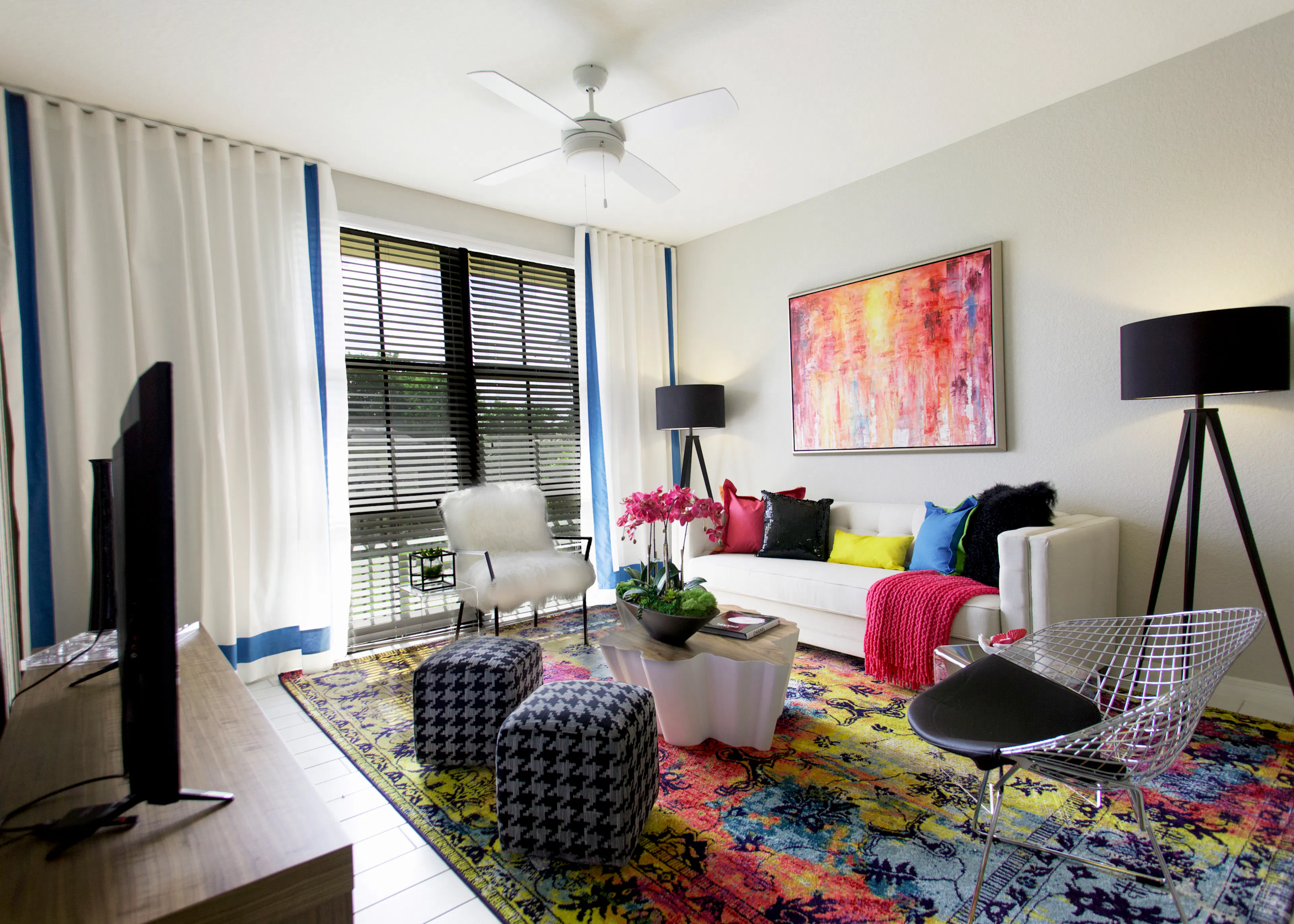 Interior of an AMLI Dadeland apartment living area with white sofa, pillows, modern colorful artwork and black floor lamps