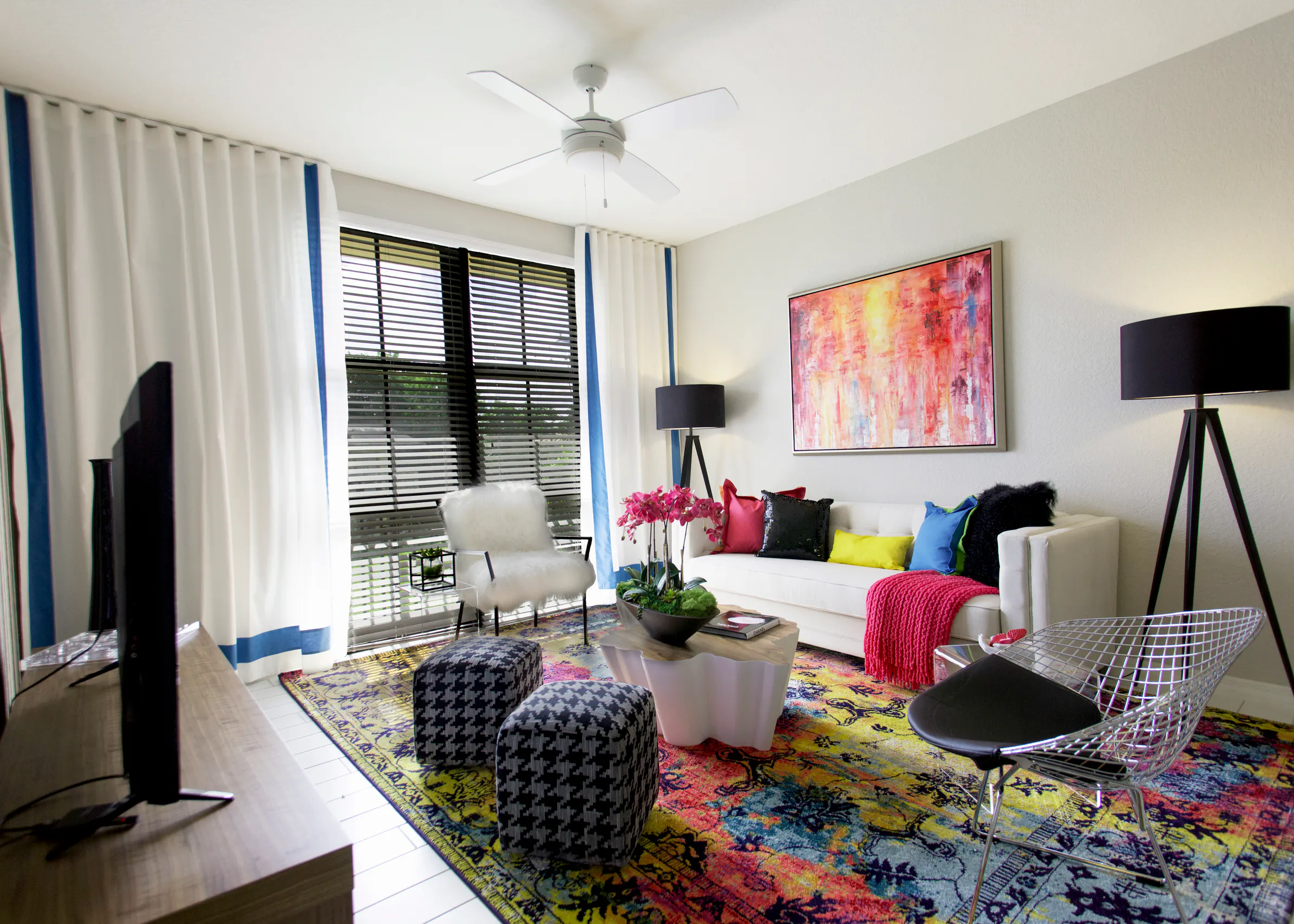 Interior of an AMLI Dadeland apartment living area with white sofa, pillows, modern colorful artwork and black floor lamps