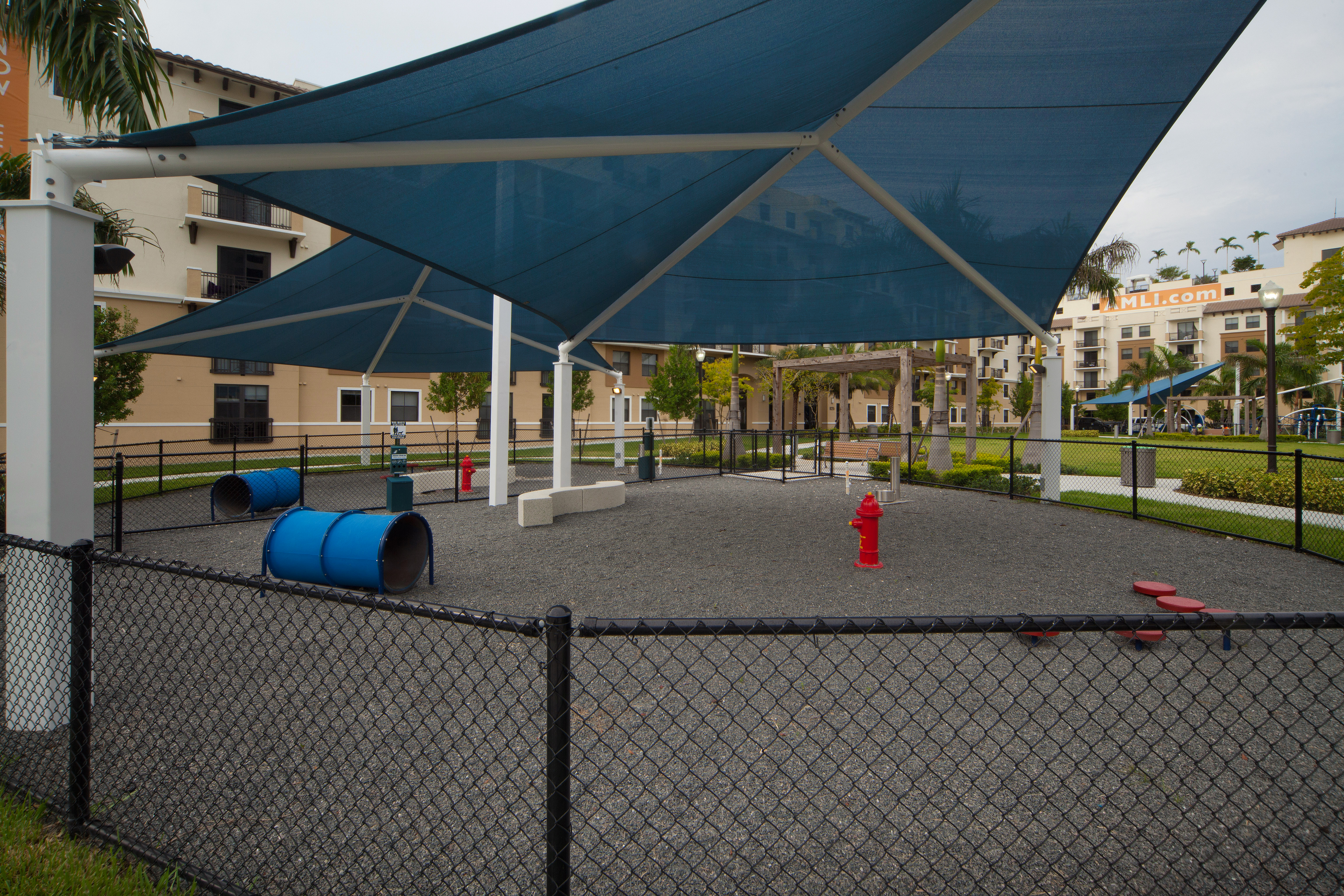 Exterior view of fully covered and gated paw park at AMLI Dadeland with agility equipment surrounded by a grassy run
