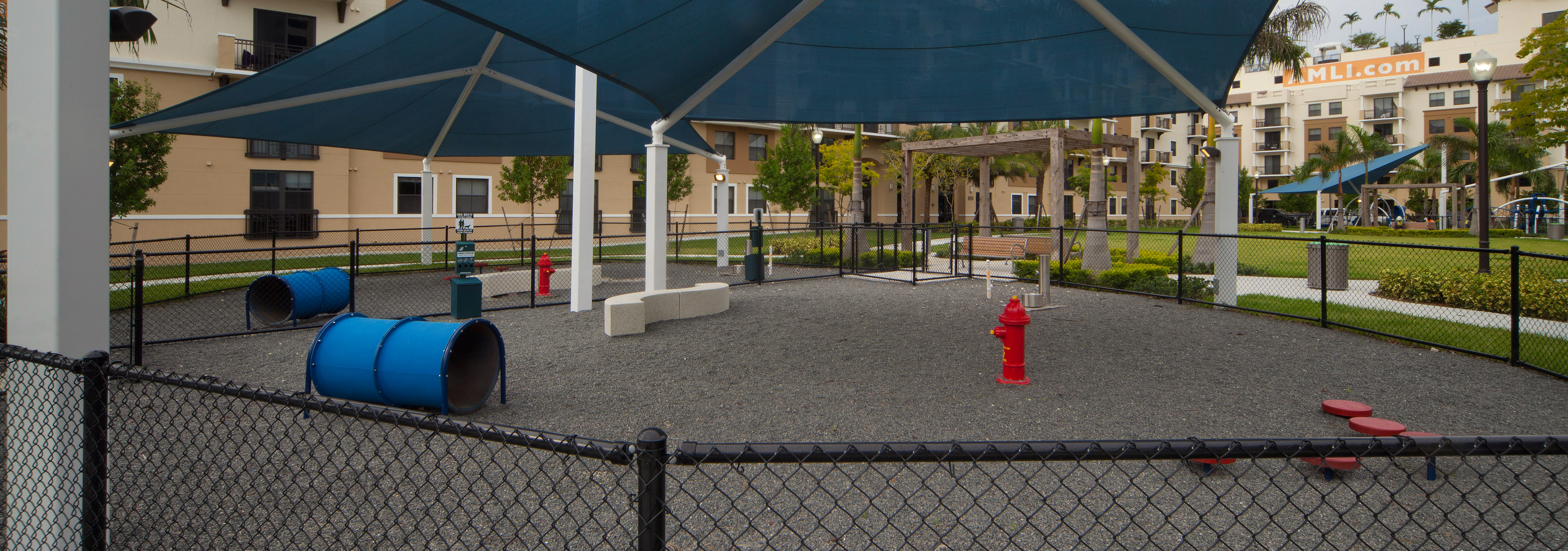 Exterior view of fully covered and gated paw park at AMLI Dadeland with agility equipment surrounded by a grassy run