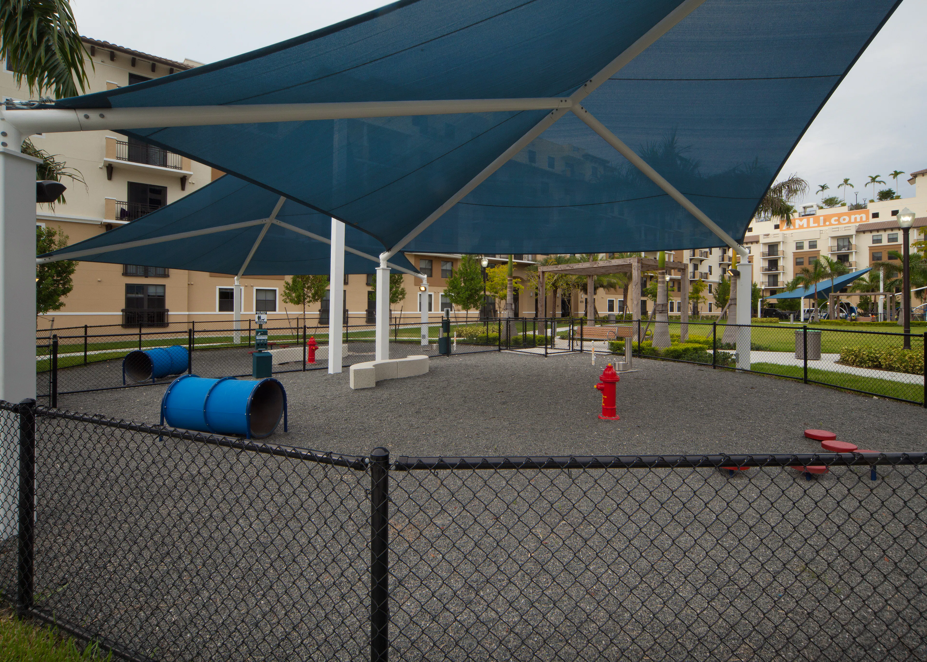 Exterior view of fully covered and gated paw park at AMLI Dadeland with agility equipment surrounded by a grassy run