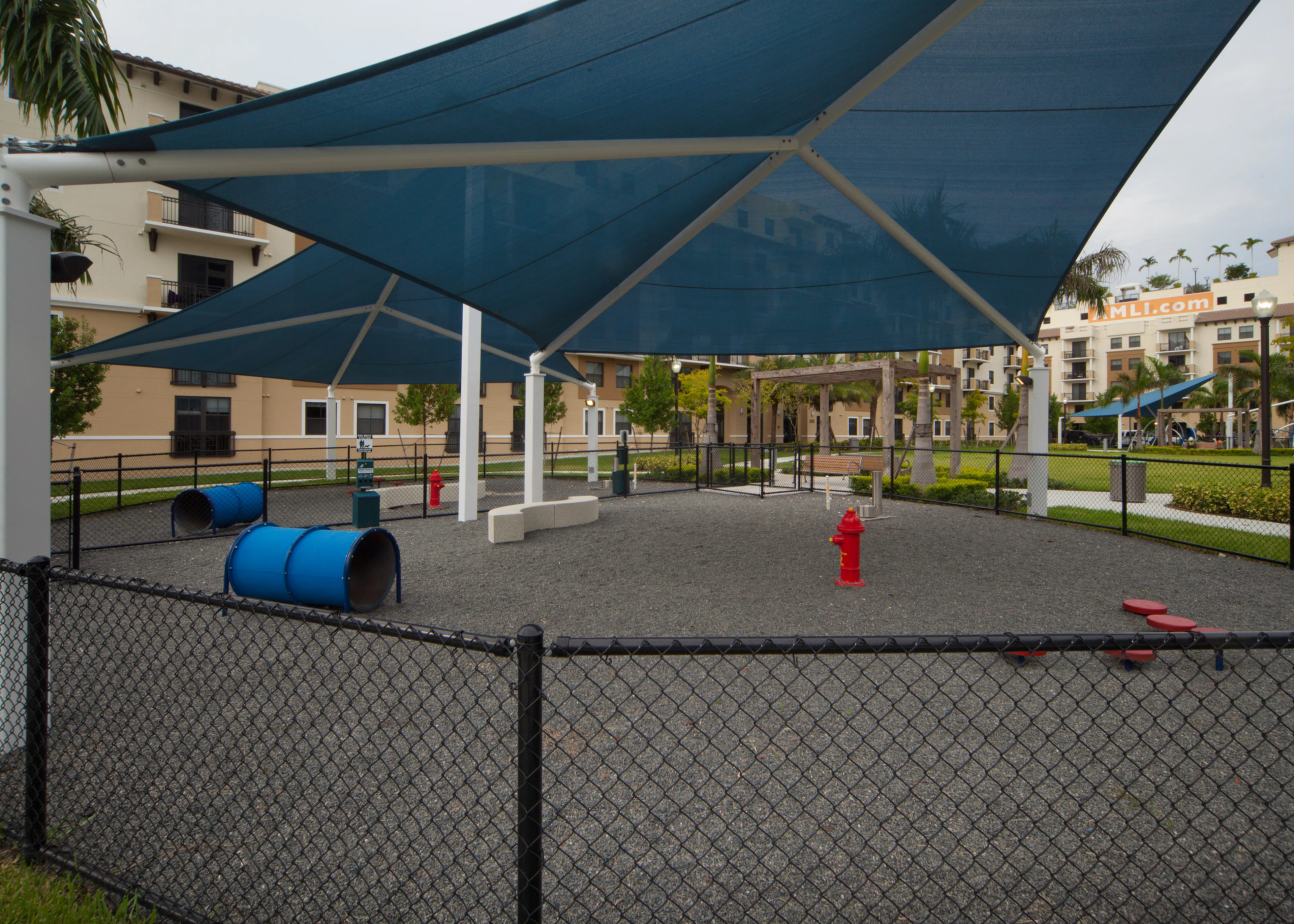 Exterior view of fully covered and gated paw park at AMLI Dadeland with agility equipment surrounded by a grassy run