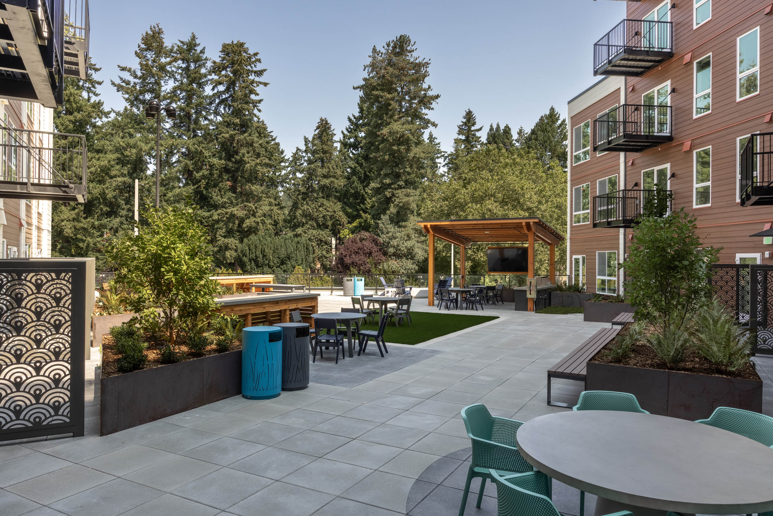 North Deck outdoor courtyard with a covered TV lounge, artificial turf, seating areas, planters, and trees surrounding the building.