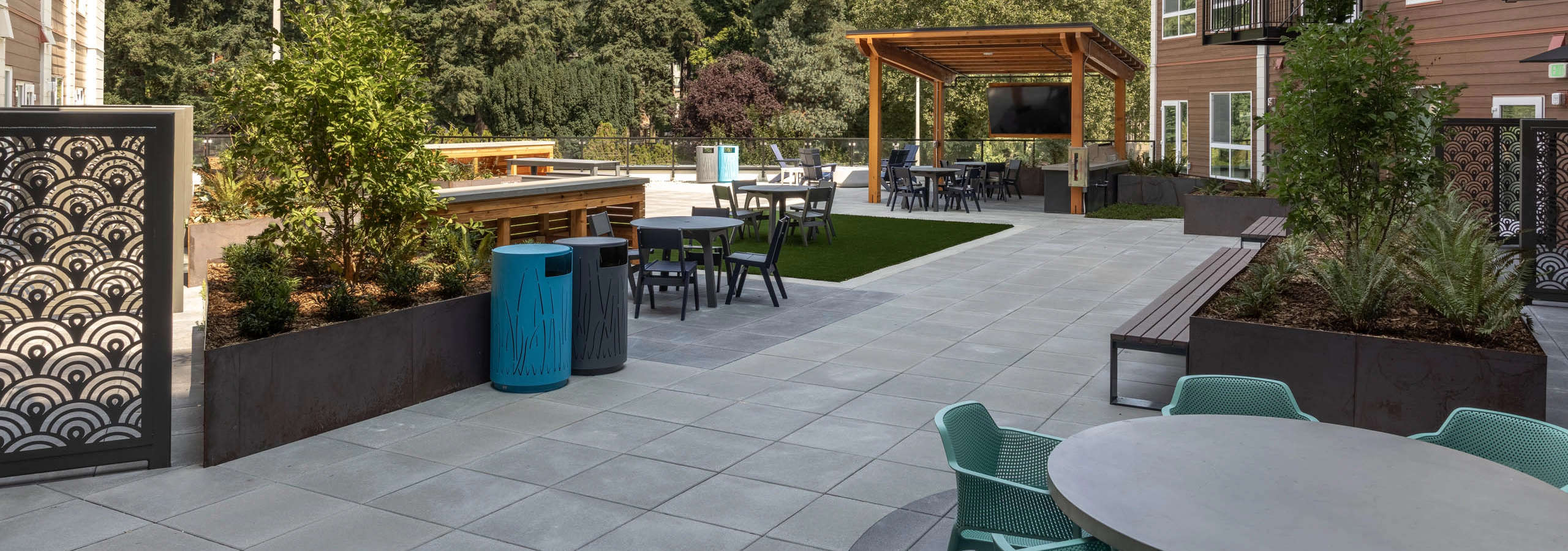 North Deck outdoor courtyard with a covered TV lounge, artificial turf, seating areas, planters, and trees surrounding the building.