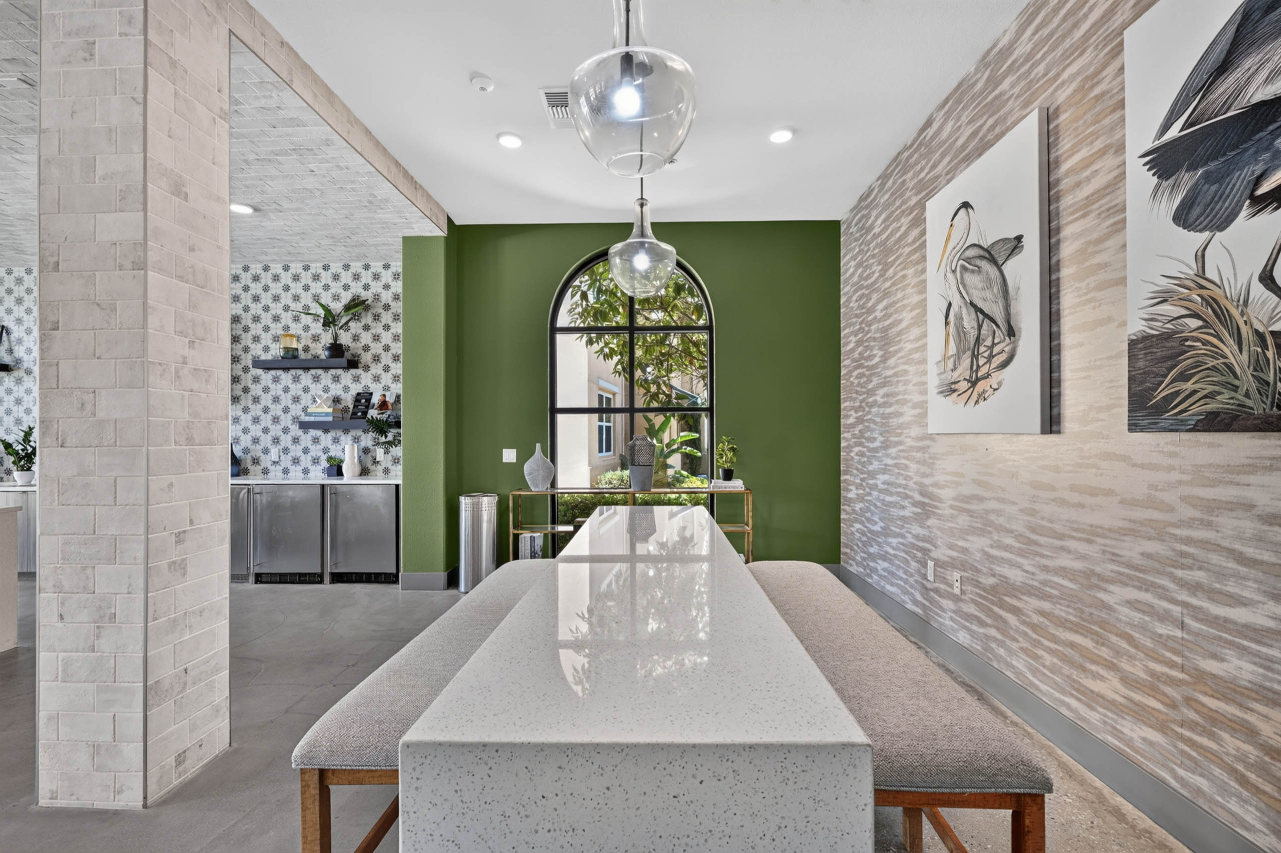  Interior view of AMLI Camarillo apartments clubhouse co-working space with long table, pendant lights, green wall and arched window.