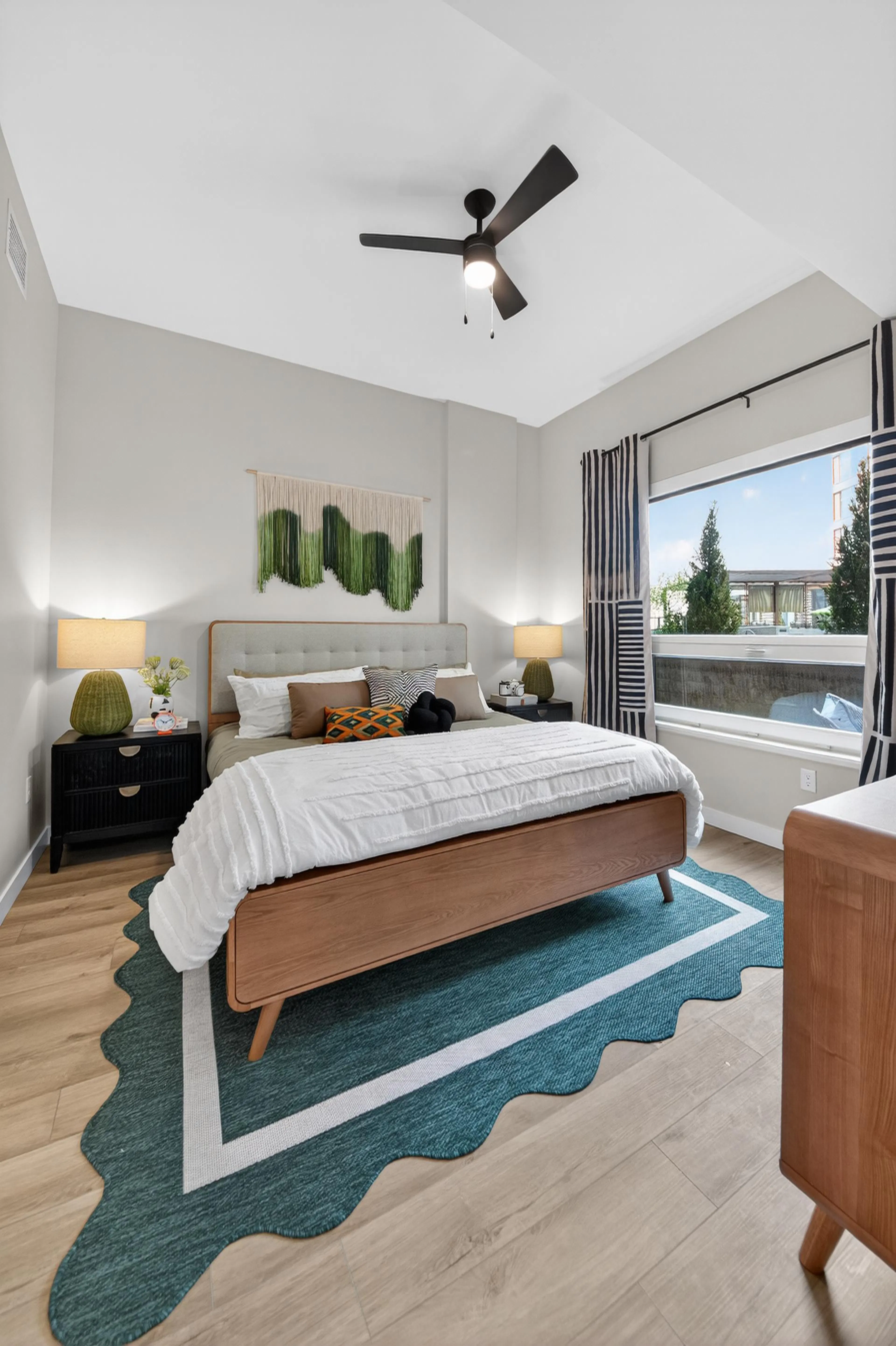 A furnished bedroom at AMLI Golden Triangle with a blue rug and wooden furniture with a white duvet set and pillows 