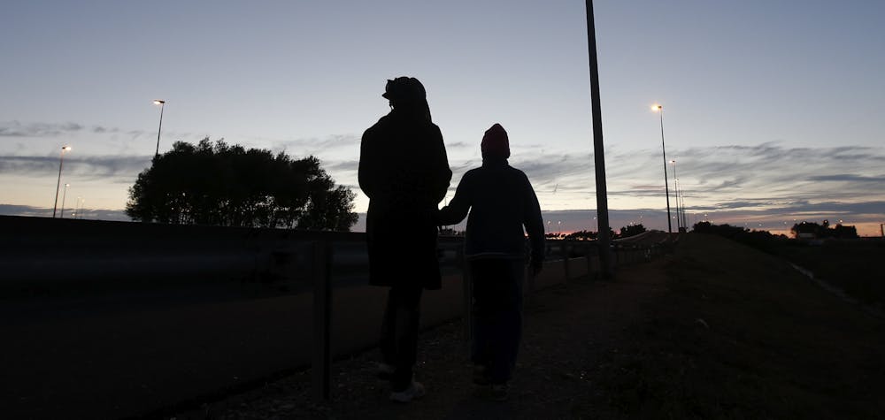 An Eritrean mother and her daughter are seen in silhouette as they walk along the motorway near the Channel Tunnel entrance near Calais, France, August 6, 2015. For most of the 3,000 inhabitants of the "Jungle", a shanty town on the sand dunes of France's north coast, the climax of each day is the nightly bid to sneak into the undersea tunnel they hope will lead to new life in Britain.