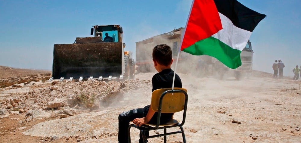  A Palestinian boy sits on a chair with a national flag as Israeli authorities demolish a school site in the village of Yatta, south of the West Bank city of Hebron and to be relocated in another area, on July 11 2018. (Photo by HAZEM BADER / AFP) (Photo credit should read 