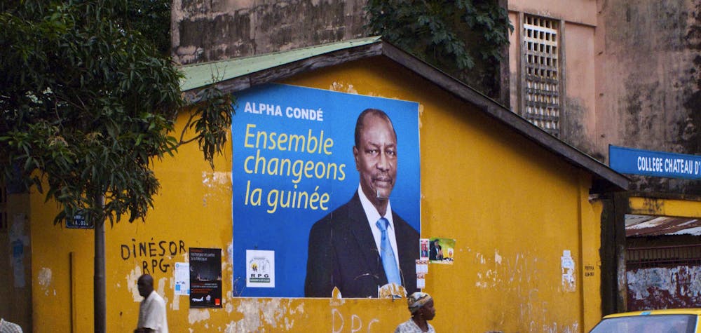 Pedestrians walk past a poster for Guinea presidential candidate Alpha Conde in Conakry, September 13, 2010. Police deployed extra forces around Guinea's capital Conakry on Monday after street fighting between supporters of rivals for its presidential election left one dead and 50 injured over the weekend. REUTERS/Joseph Penney (GUINEA - Tags: POLITICS ELECTIONS)