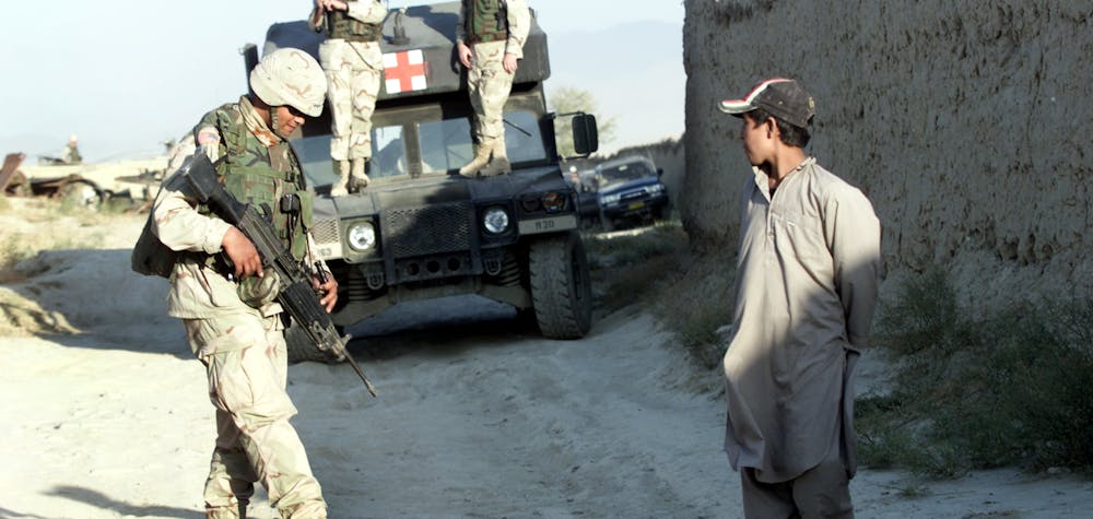 An Afghan boy watches U.S. soldiers at a check point near the site of a blast outside the U.S. headquarters at Bagram north of Kabul on October 3, 2003. At least four Afghans were killed and two were missing after the blast outside the main base of U.S. forces in Afghanistan, which a U.S. officer said may have been caused by children playing with bombs. 