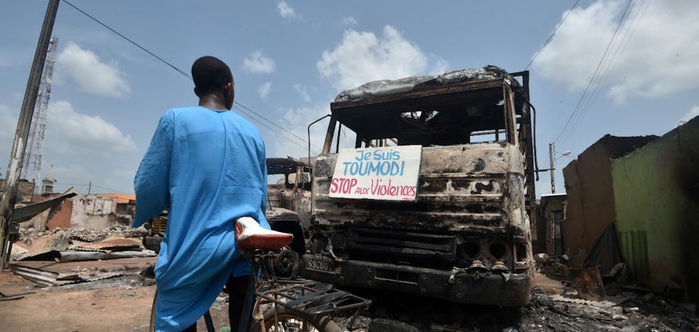 A cyclist reads a sign on a burnt truck calling for violence to stop in the market of Toumodi on November 4, 2020, during a campaign of non-violence and peace awareness by young volunteers after inter-community clashes during the country's presidential election of October 31, 2020. - Ivory Coast is caught in a standoff after Ivorian President Alassane Ouattara won a third term by a landslide in October 31, 2020's vote, which was boycotted by the opposition claiming an "electoral coup" in a nation with a constitutional two-term presidential limit. (Photo by SIA KAMBOU / AFP)