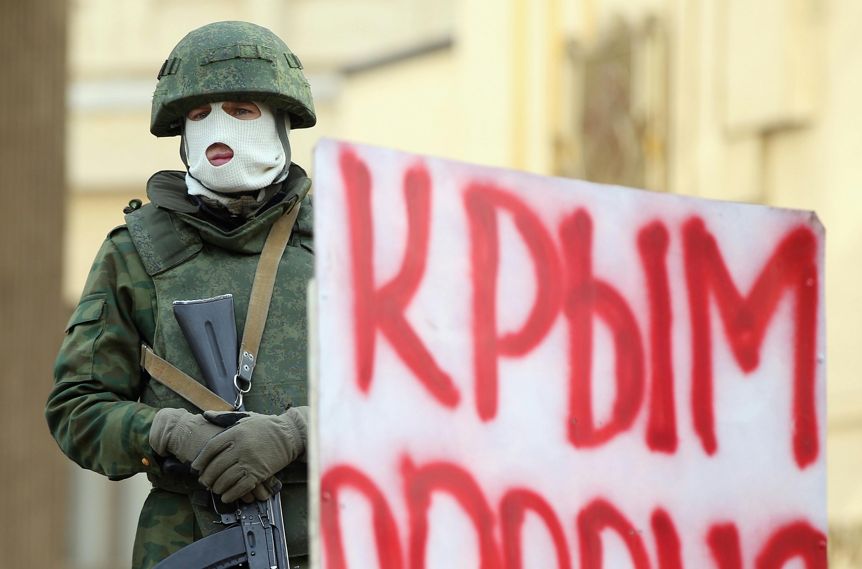 SIMFEROPOL, UKRAINE - 01 MARS : Un soldat lourdement armé sans insigne d'identification
garde le bâtiment du parlement de Crimée à côté d'un panneau indiquant : "Crimée Russie" après que plusieurs dizaines de soldats y ont pris position plus tôt dans la journée du 1er mars 2014 à Simferopol,
Ukraine.