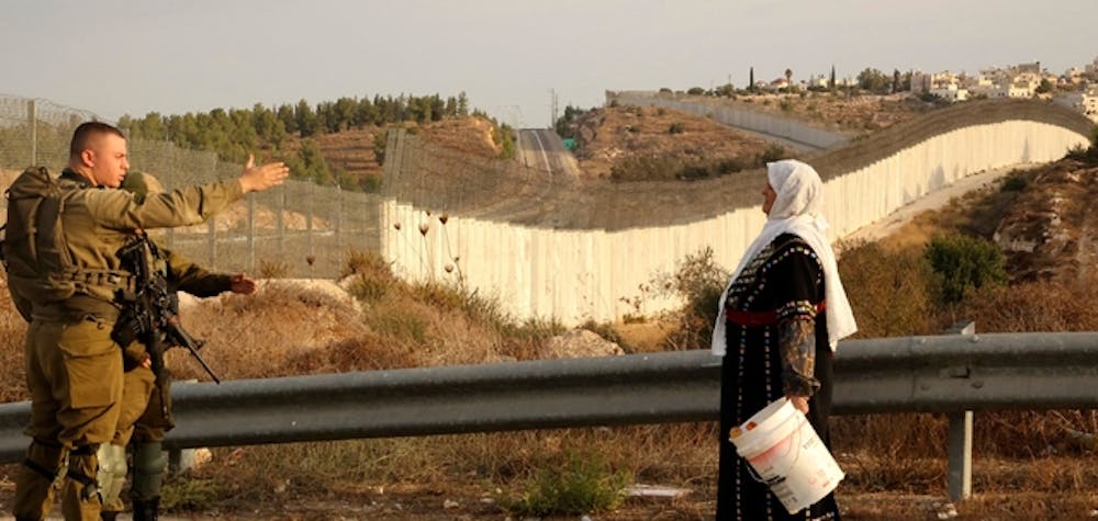 A Palestinian woman stands with others (not pictured) as they gather near an Israeli army checkpoint as they wait to reach their olives fields on the other side of Israel's separation barrier (background) after they received an special Israeli permission to harvest their olive trees, on October 13, 2021 near Bait A'wa village on the outskirts of the West Bank city of Hebron. (Photo by HAZEM BADER / AFP) (Photo by HAZEM BADER/AFP via Getty Images)