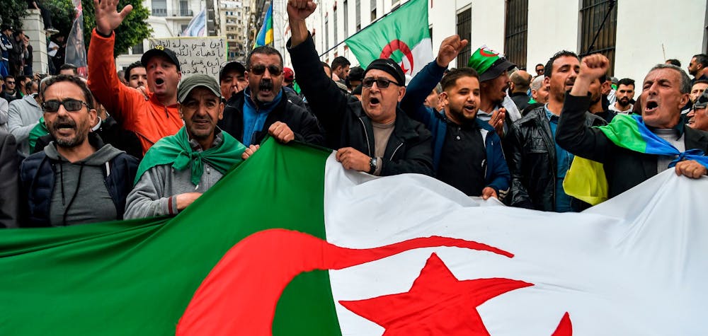  	People chant slogans as they wave a large Algerian national flag during a weekly anti-government demonstration in the capital Algiers on March 6, 2020. - Protests against cronyism have continued in Algeria despite former president Abdelaziz Bouteflika's resignation and the election of a new president in December 2019.