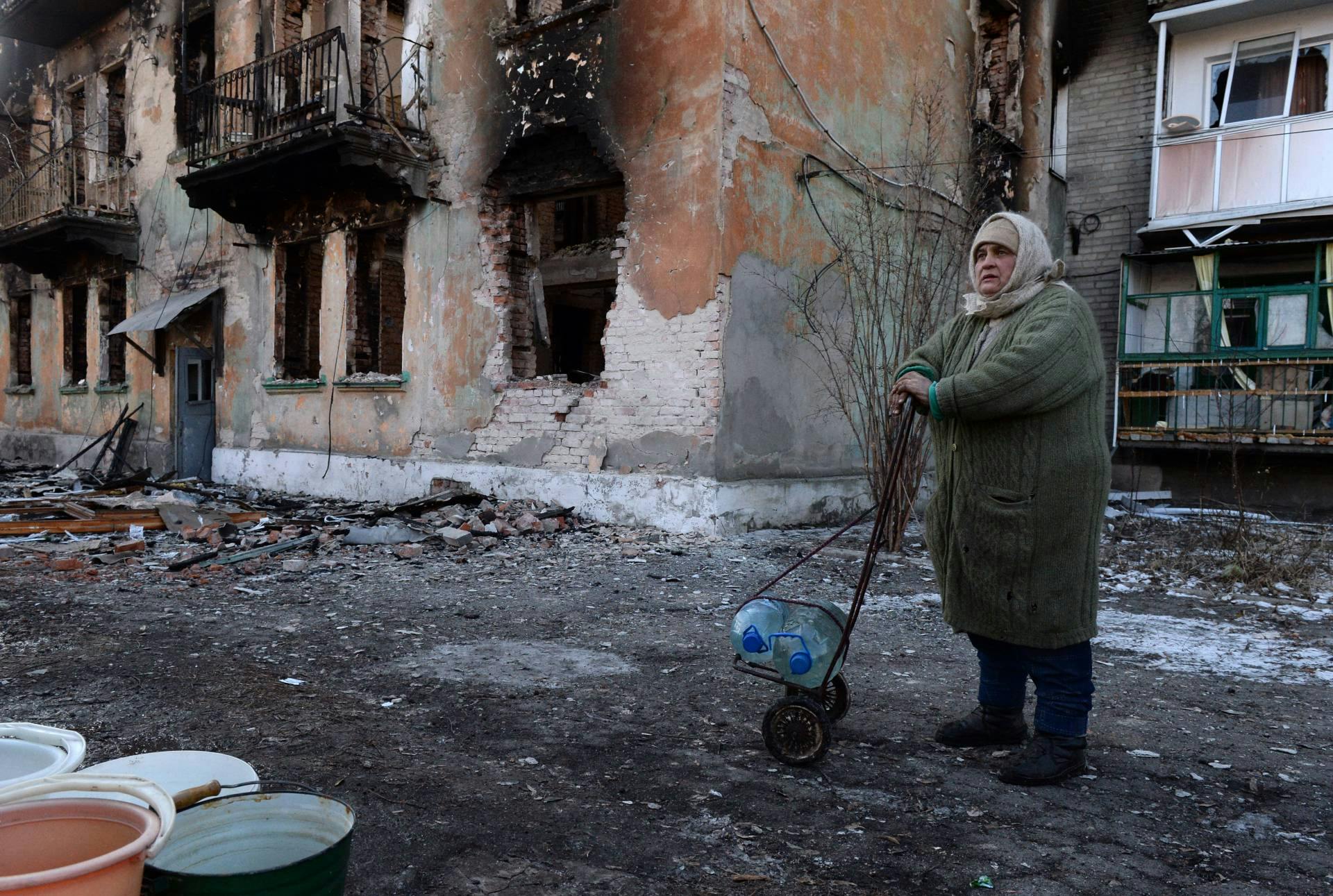 A local woman uses a shopping trolley to carry water containers past a damaged building in the eastern Ukrainian city of Debaltseve in the Donetsk region, on February 20, 2015. The leaders of Ukraine, Germany, France and Russia on February 20 pledged renewed support for a tattered ceasefire in eastern Ukraine despite violations -- including the storming of a key town by pro-Russian rebels. 