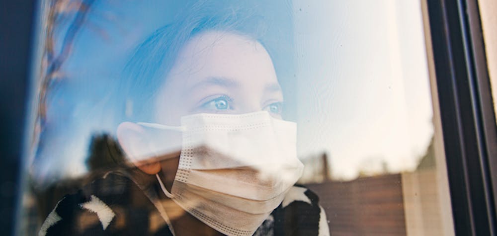 Young girl with mask looking through window
