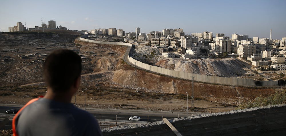 A picture taken on October 18, 2016 from the east Jerusalem Arab neighbourhood of Issawiya shows a Palestinian youth looking on as the Palestinian Shuafat refugee camp (R) is seen behind the controversial Israeli separation wall. (Photo by AHMAD GHARABLI / AFP)