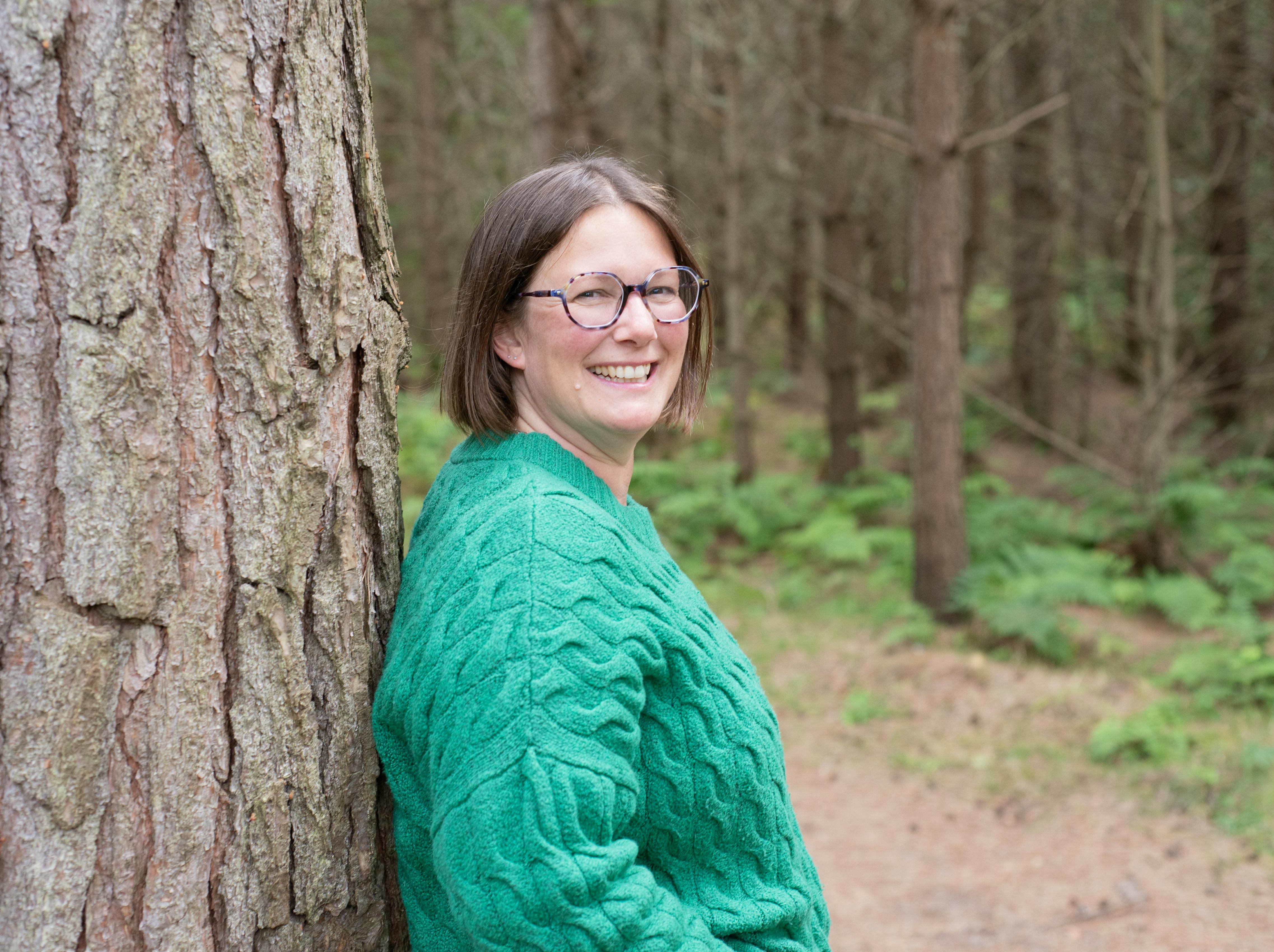 Amy standing leaning against tree