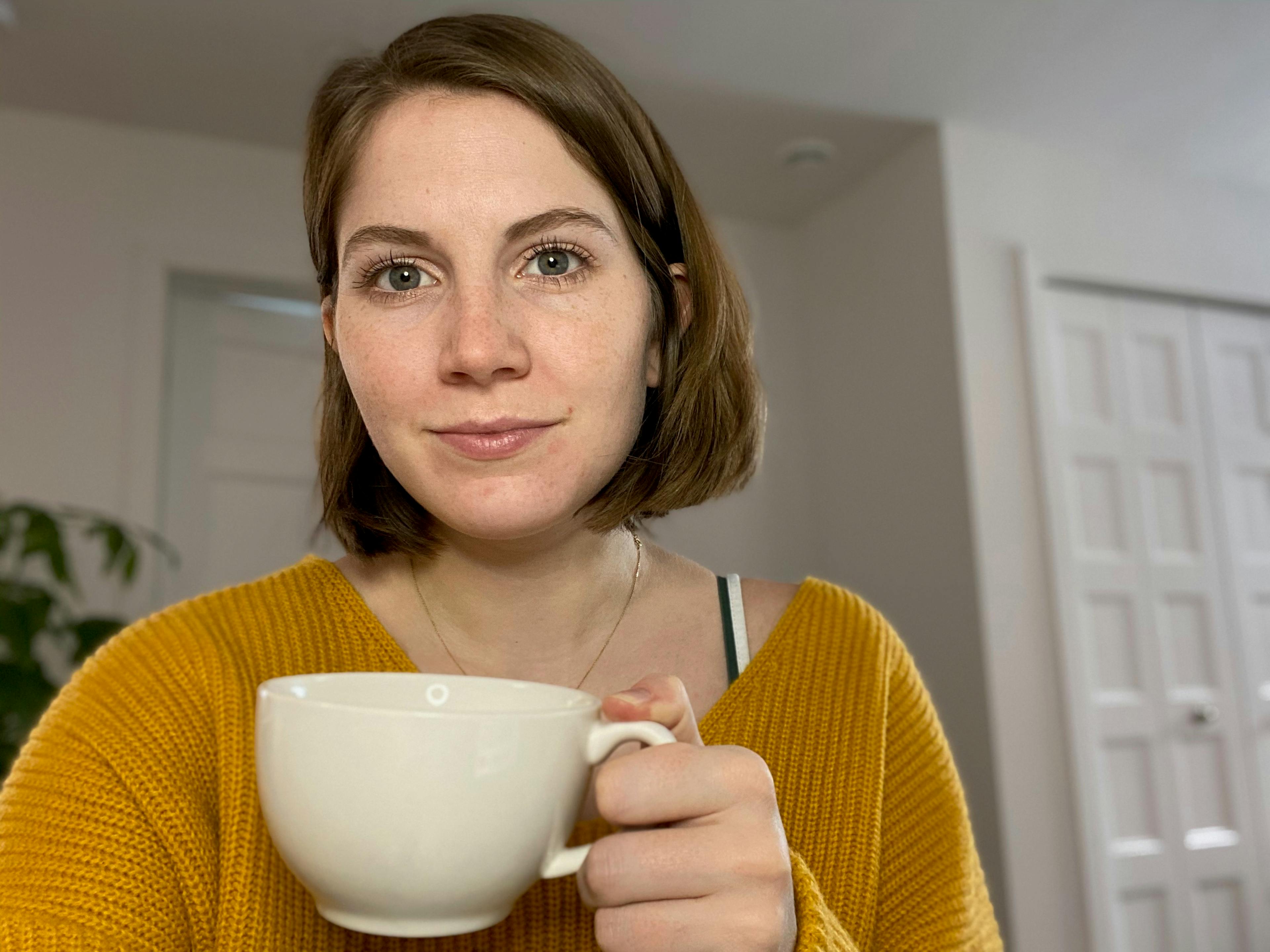 selfie of a woman with short, brown hair holding a white latte mug. 