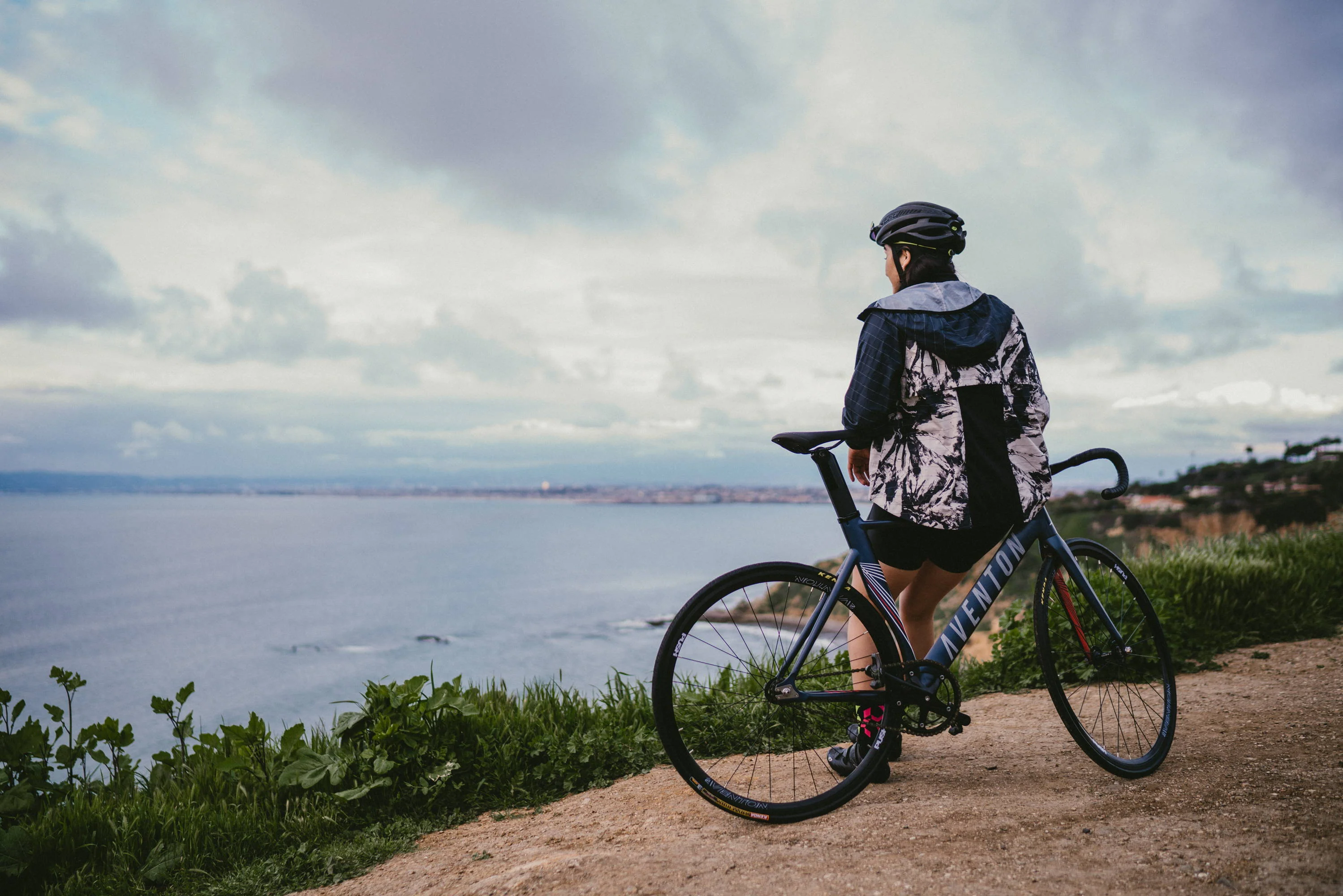Image of a woman leaning against an Aventon bike looking out a coastline 
