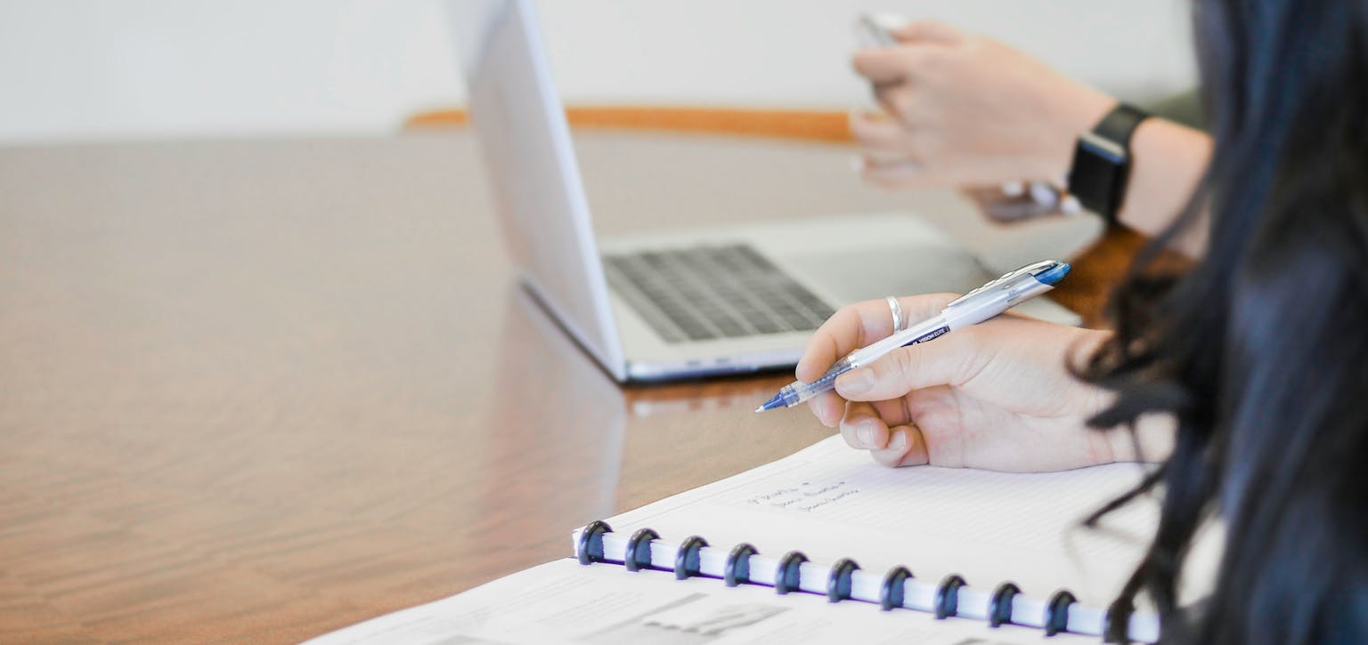 People sitting at desk next to laptop and notebook