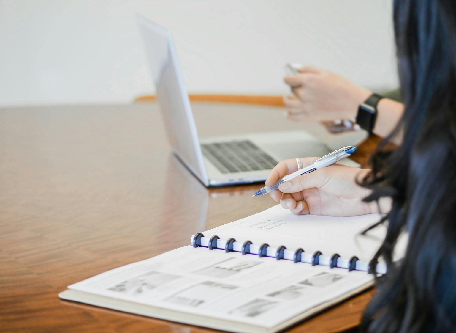 People sitting at desk next to laptop and notebook