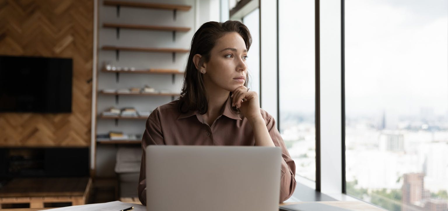 Woman at desk, thinking and looking out of window